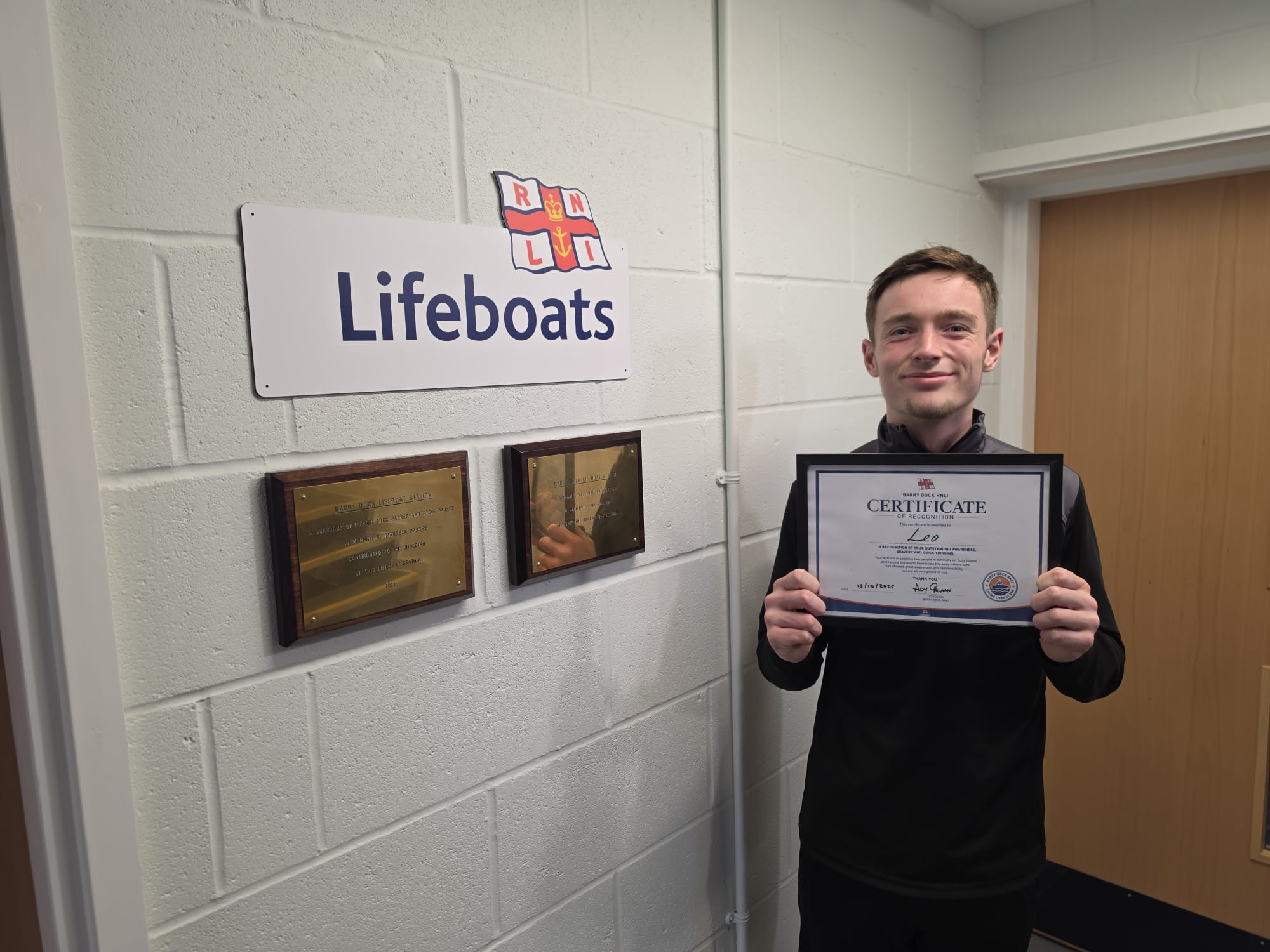 A young man holding a certificate by an RNLI Lifeboats sign 