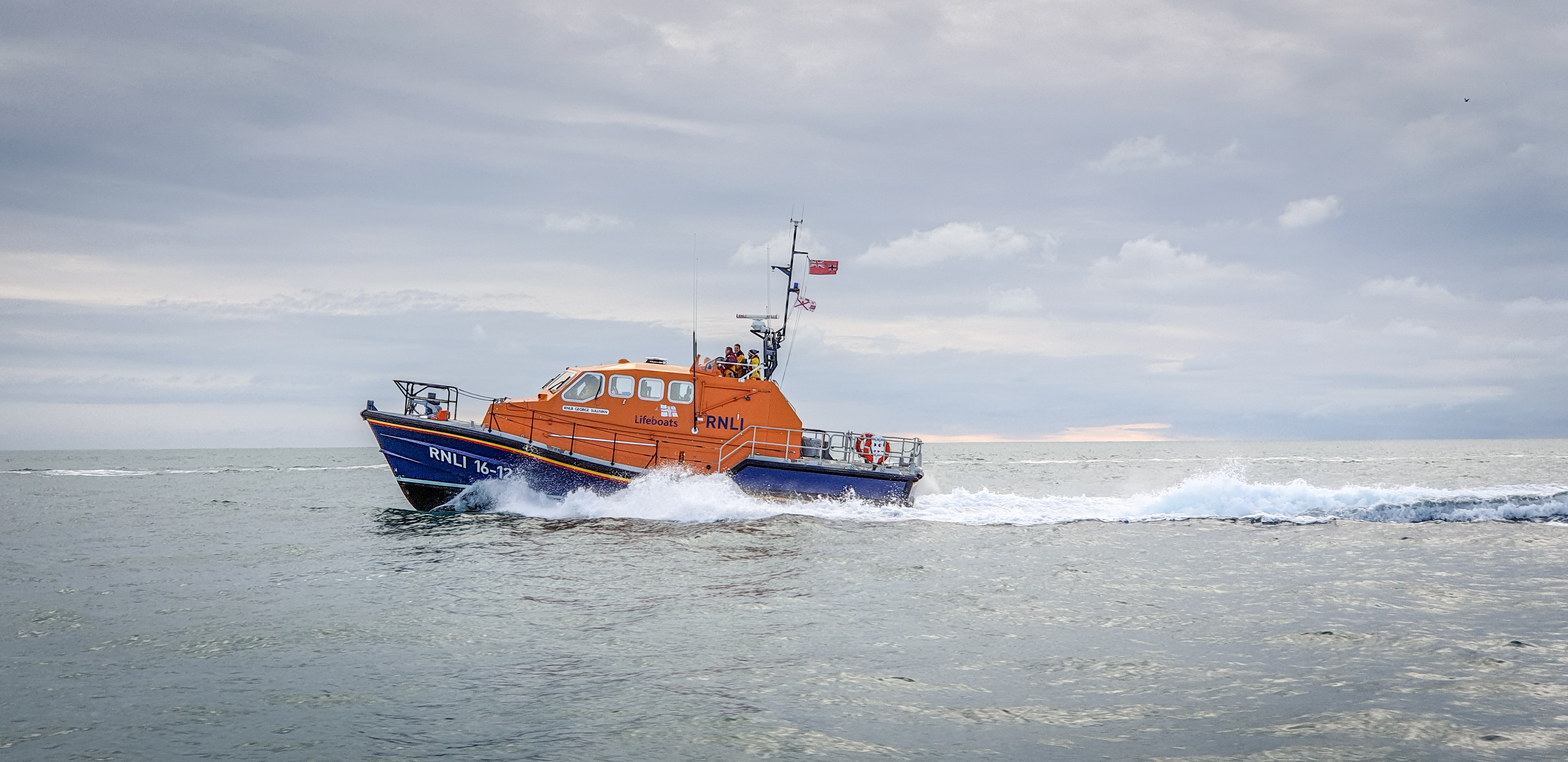 The St Helier Tamar class all weather lifeboat at sea and moving at pace under a moody sky