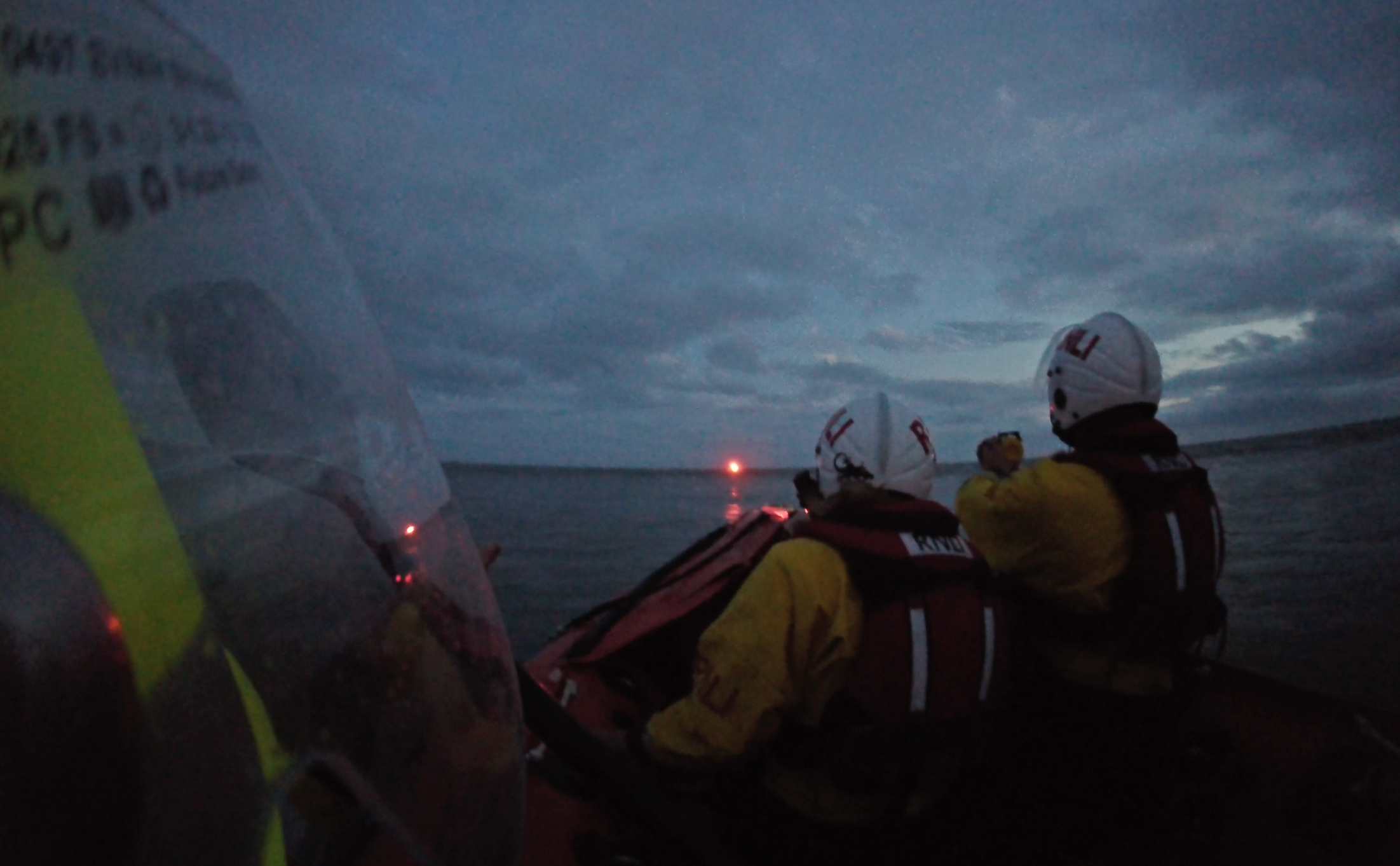 Two volunteer crew point to a flare in the distance 