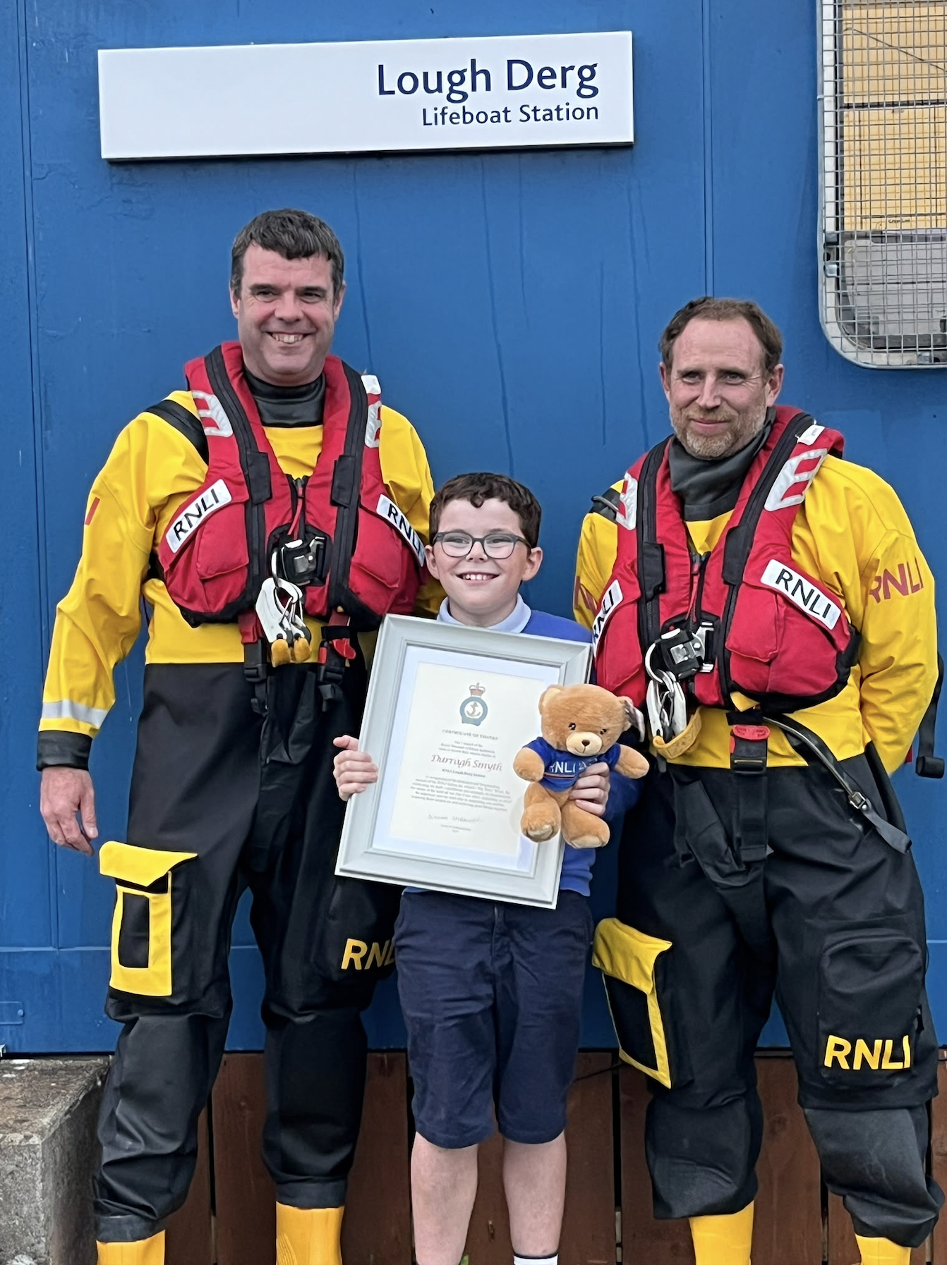 Steve and Owen, brothers-in-law and Darragh, Steve's son are standing in a group outside the station, Darragh is proudly holding his RNLI Certificate of Thanks