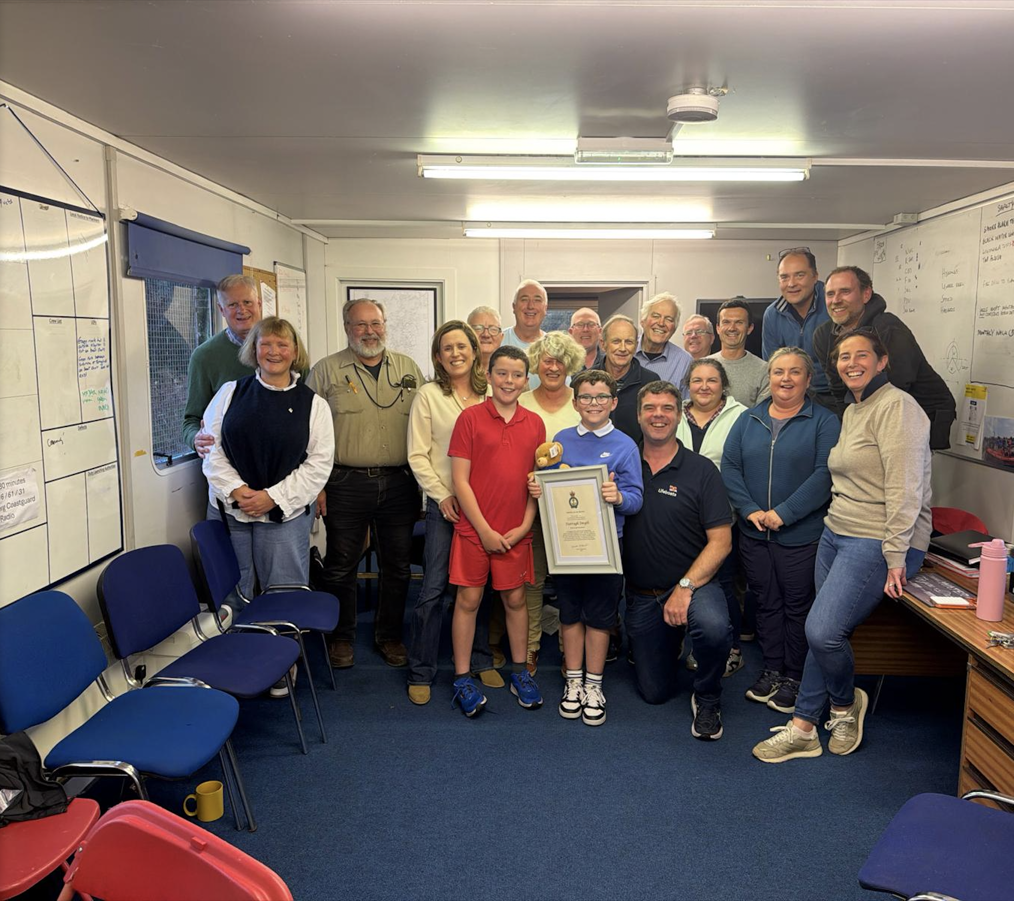 A group photograph of Lough Derg RNLI volunteers inside the station with Darragh holding his RNLI Certificate of Thanks