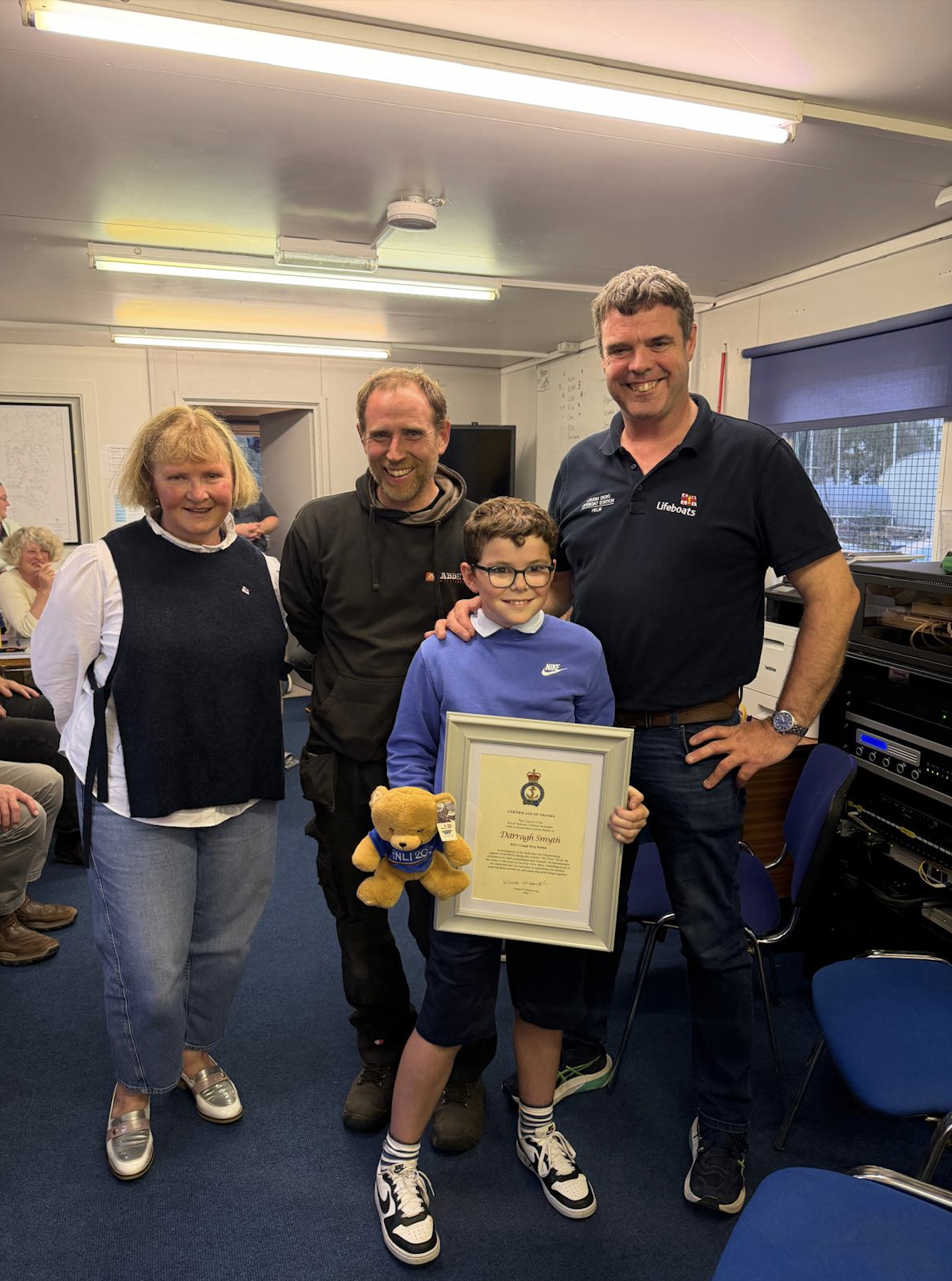 A group photograph of Darragh Smyth holding his framed Certificate of Thanks and RNLI200 teddy bear, behind his are volunteer Eleanor Hooker, his uncle Owen Cavanagh and Steve, his Dad