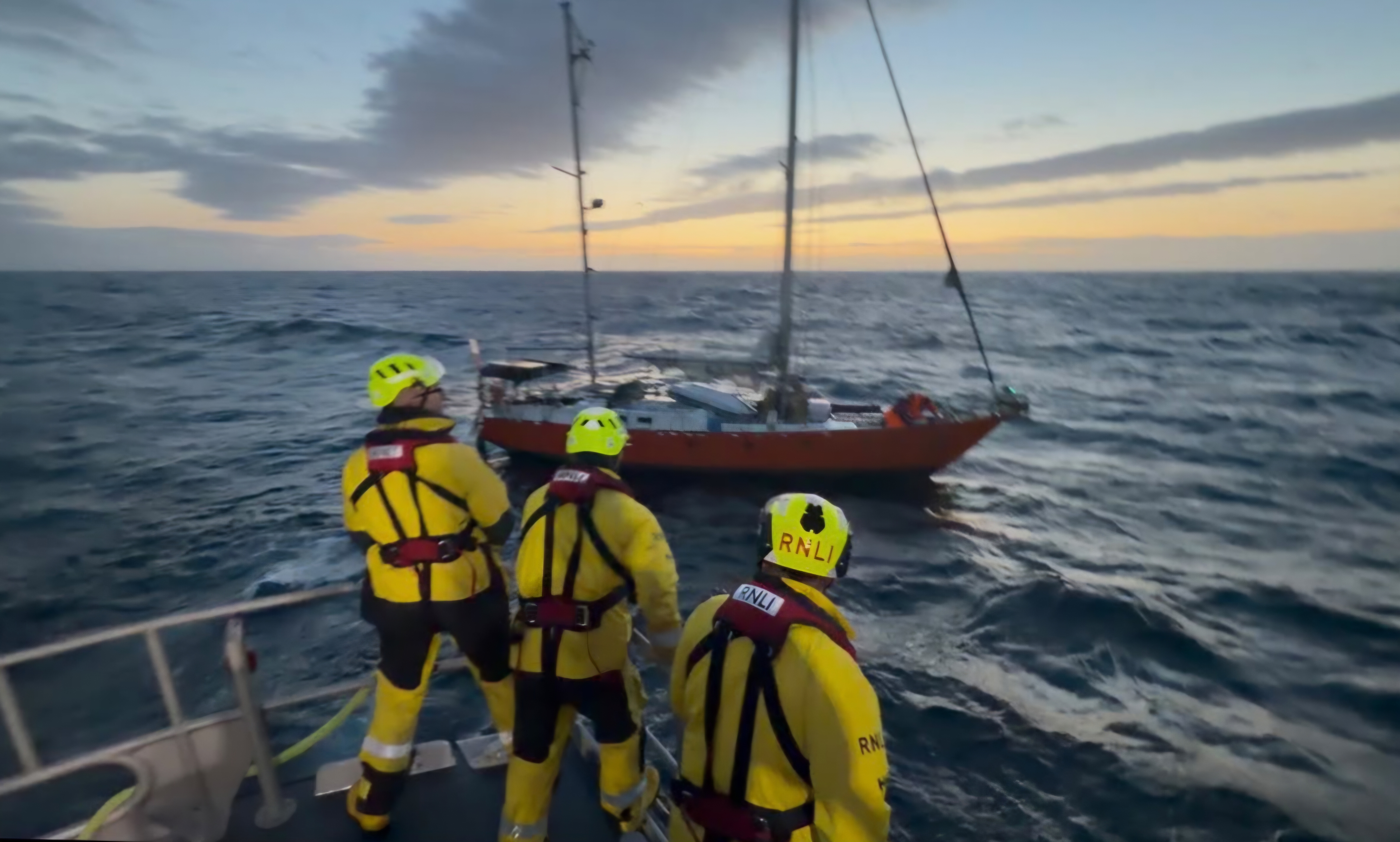 Three lifeboat crew in yellow on deck as they approach a yacht.