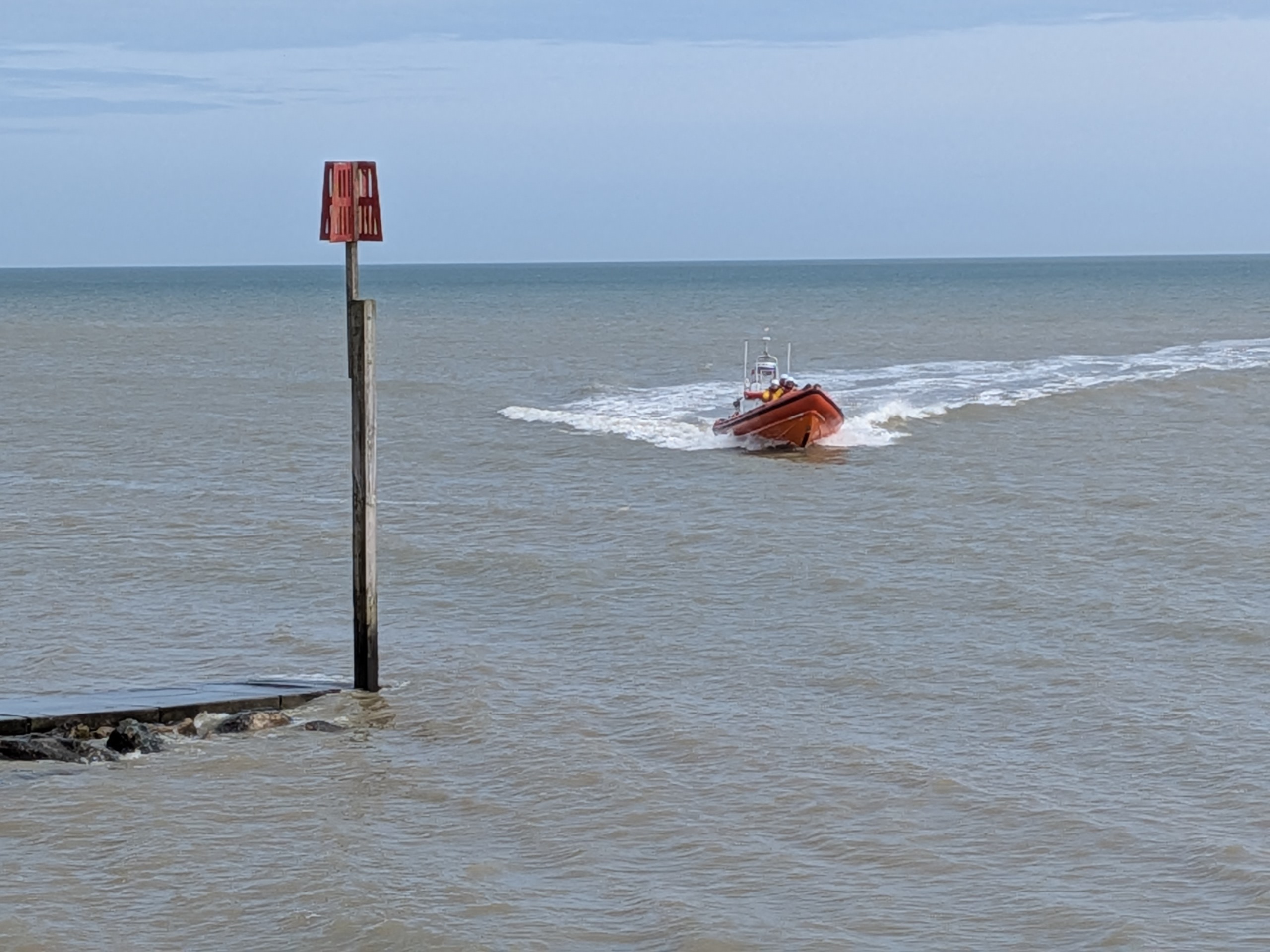 An orange lifeboat with surf behind it speeding close towards.the shoreline 
