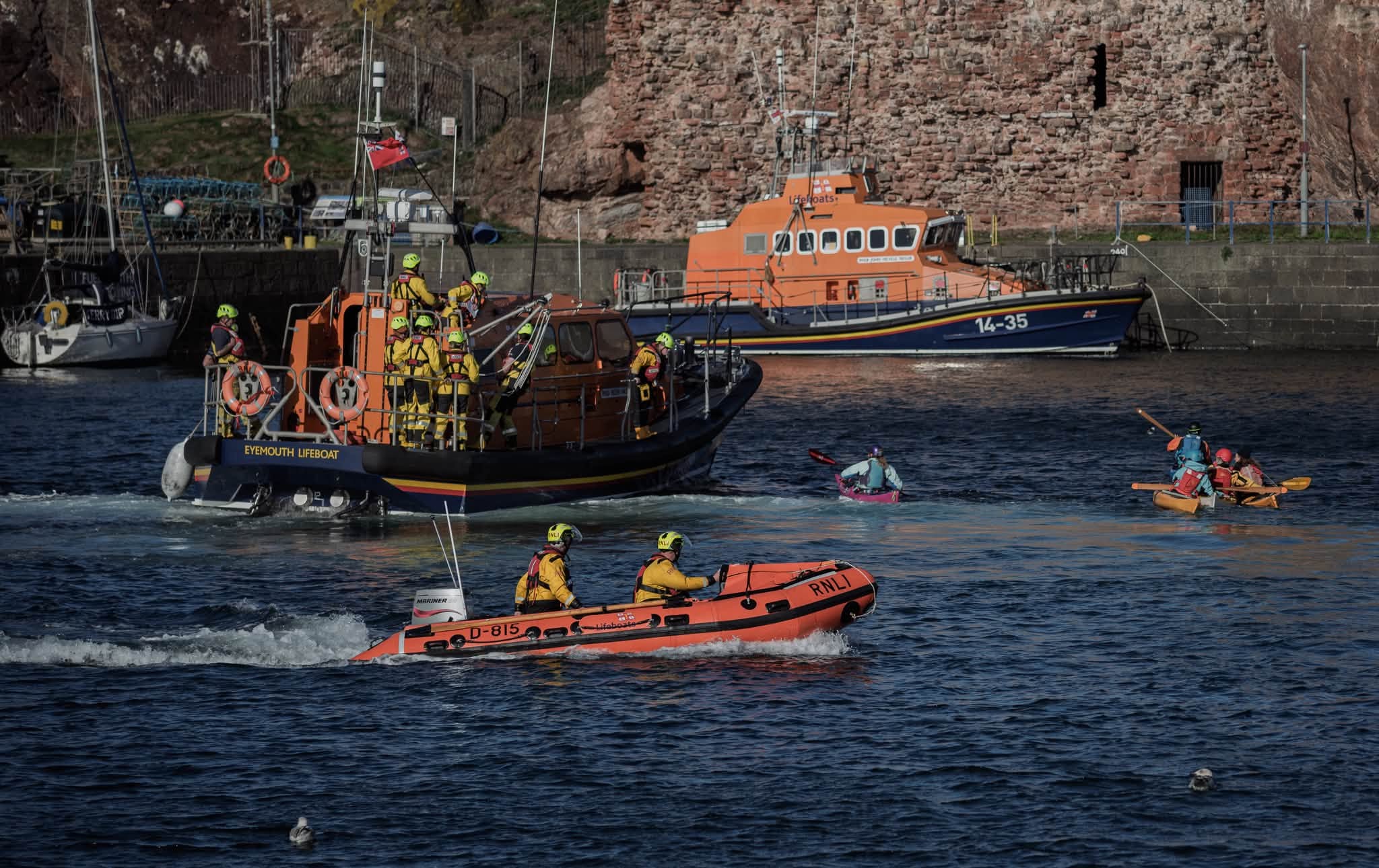 Three lifeboats and kayakers in harbour.