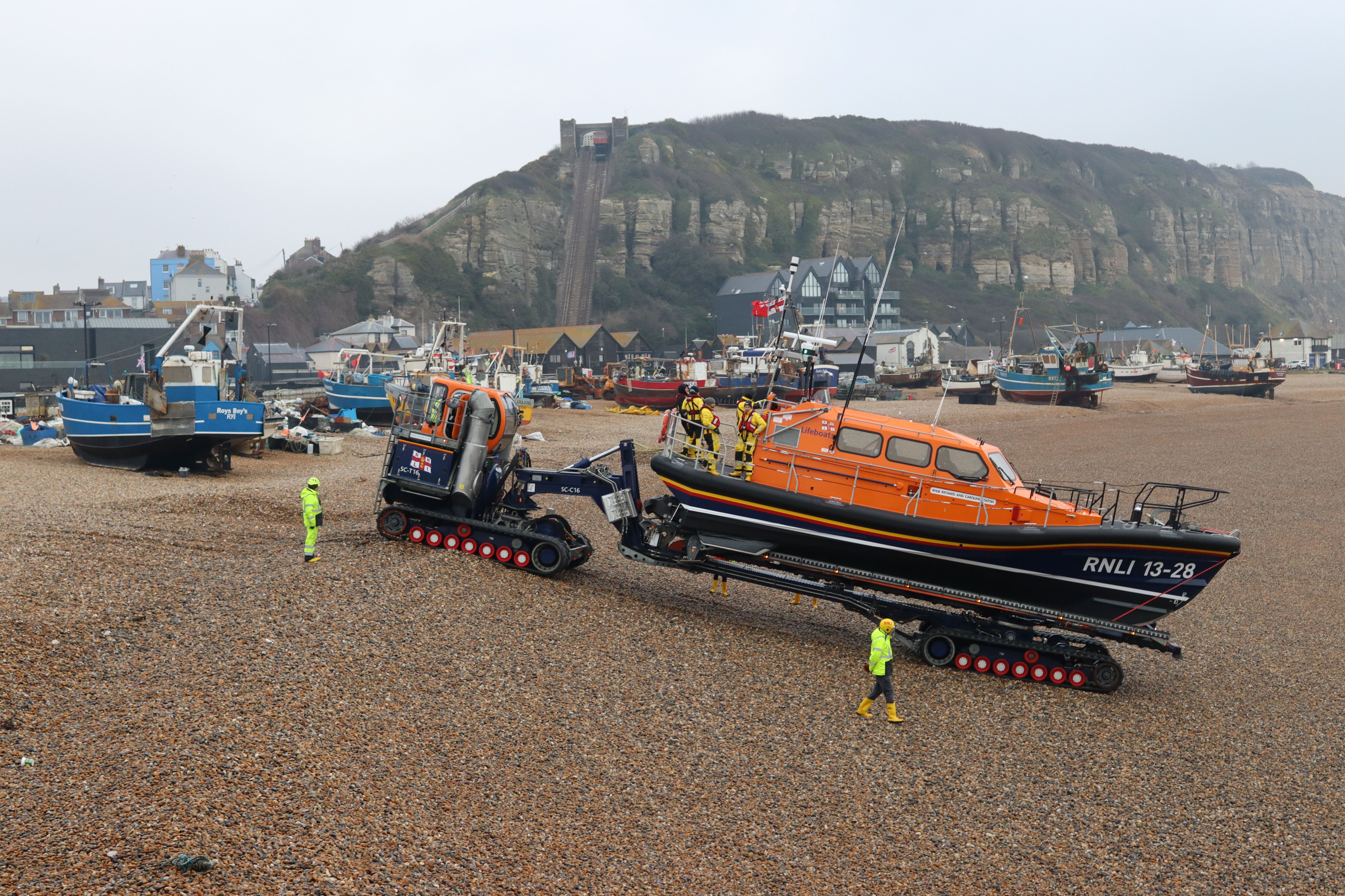 Hastings lifeboat being pushed down the beach at Hastings, with fishing boats and cliff behind