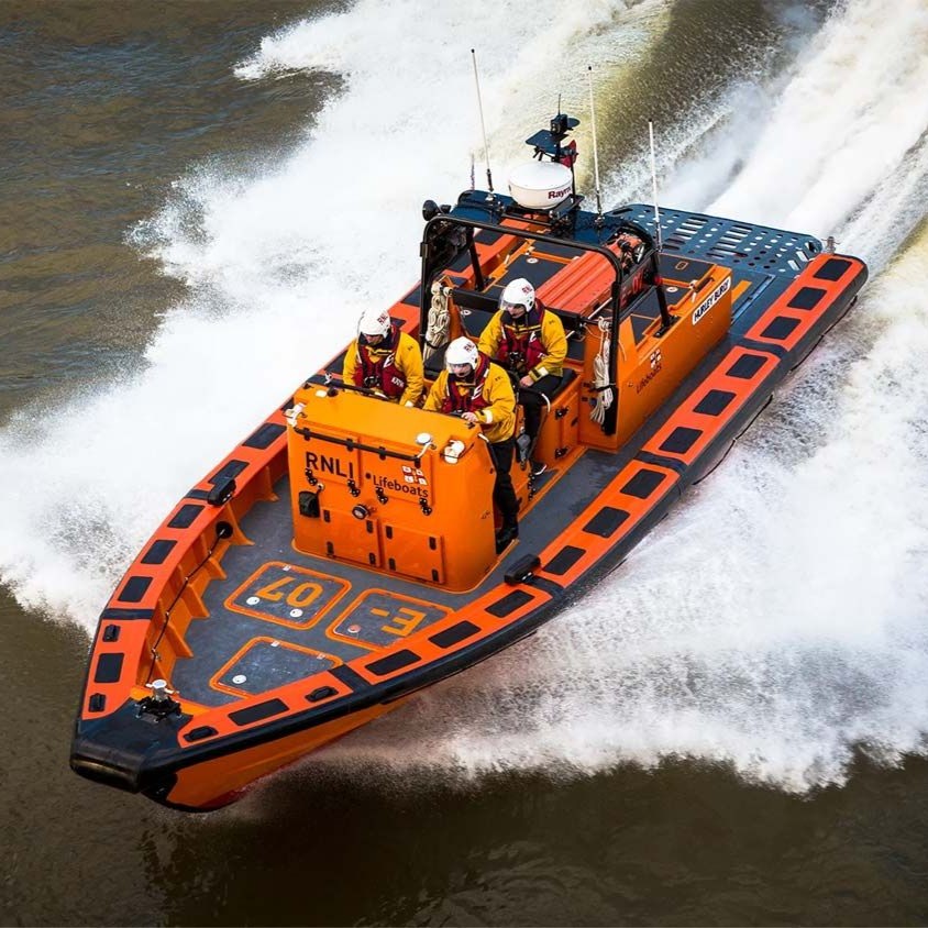 An E-class lifeboat with three crew members powering through the water.