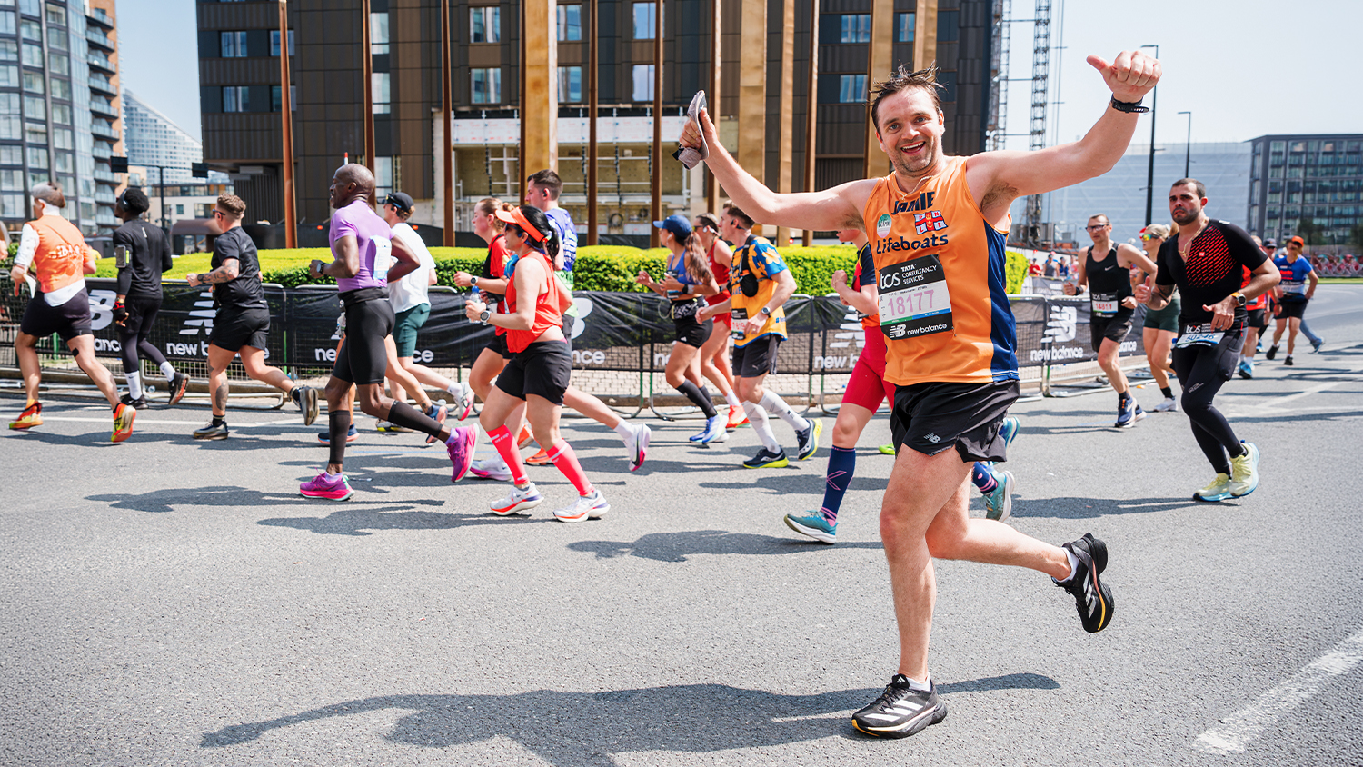 London marathon runners on the route, with a man running for the RNLI smiling and giving the thumbs up to the crowd. 