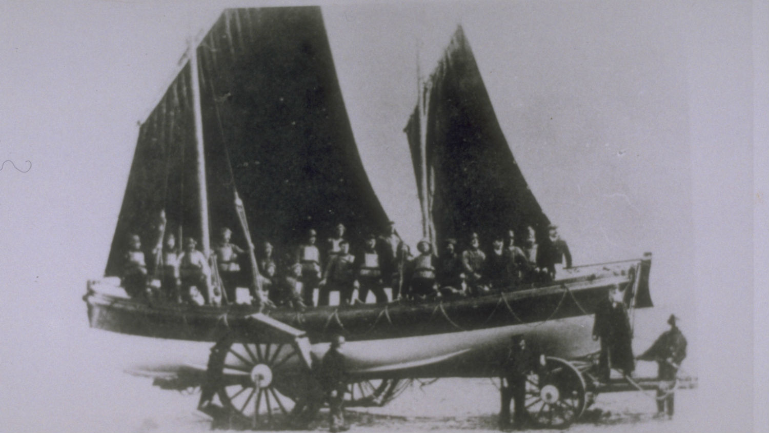Cromer lifeboat Louisa Heartwell on her carriage. The crew are wearing lifejackets and holding oars aloft. 