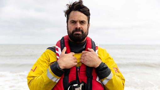 RNLI crew member Dan Sinclair poses for a photo wearing yellow inshore lifeboat gear and a bright red RNLI lifejacket