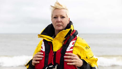 RNLI crew member Panda Lain poses for a photo wearing yellow inshore lifeboat gear and a bright red RNLI lifejacket