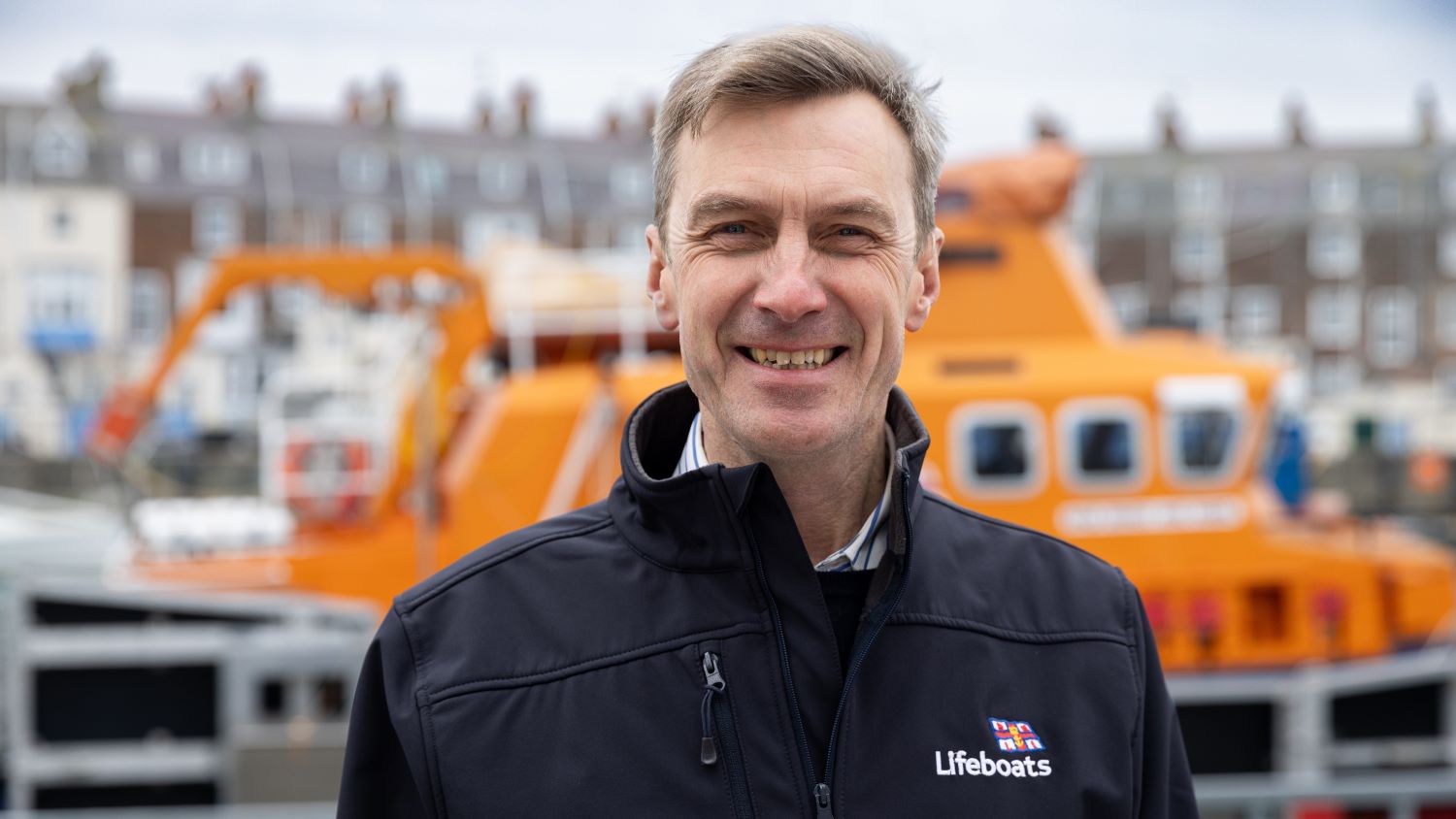 Smiling headshot of Peter Sparkes, RNLI CEO, standing in front boat in black jacket.