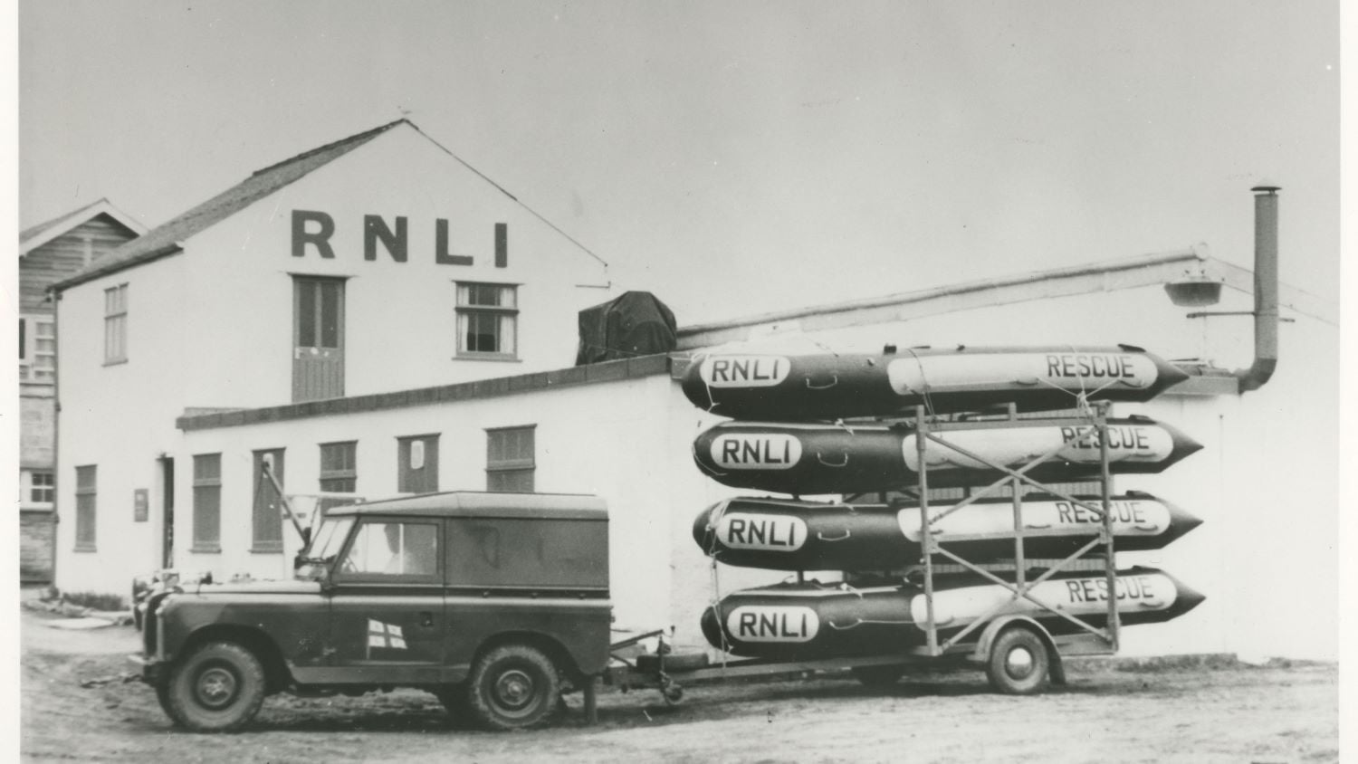 Black and white image of landrover with four inflatable rescue boats on trailer