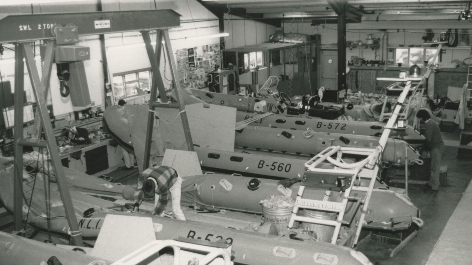 Black and white image of workshop interior with inflatable lifeboats being manufactured