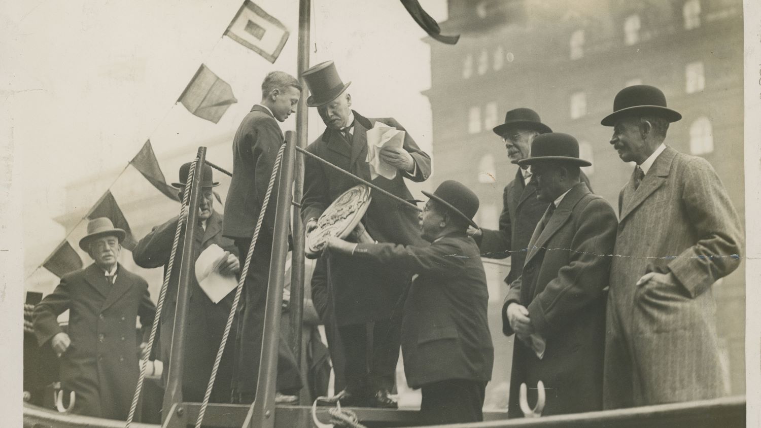 Black and white image of boy being presented with competition shield onboard lifeboat
