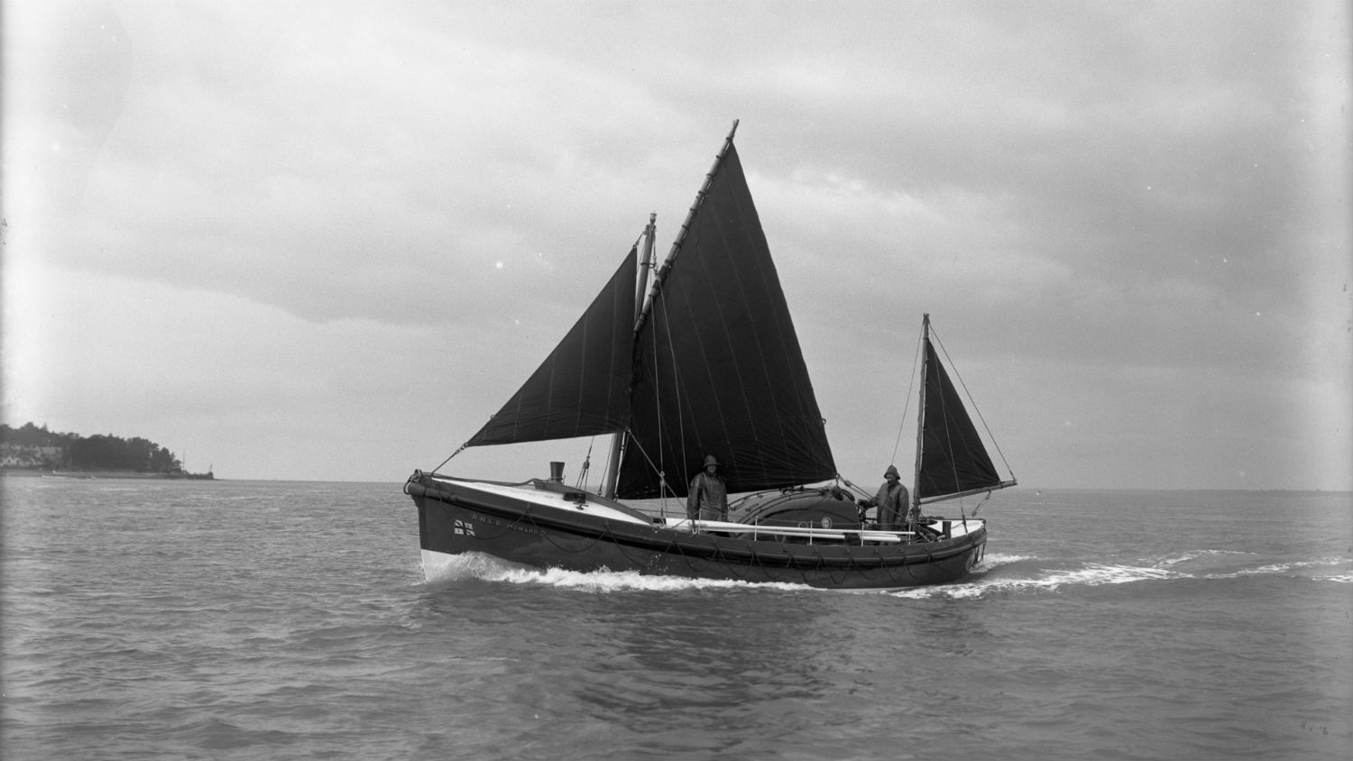 A black and white image of St Helier lifeboat, Howard D, out at sea on trials, with it's sail up.