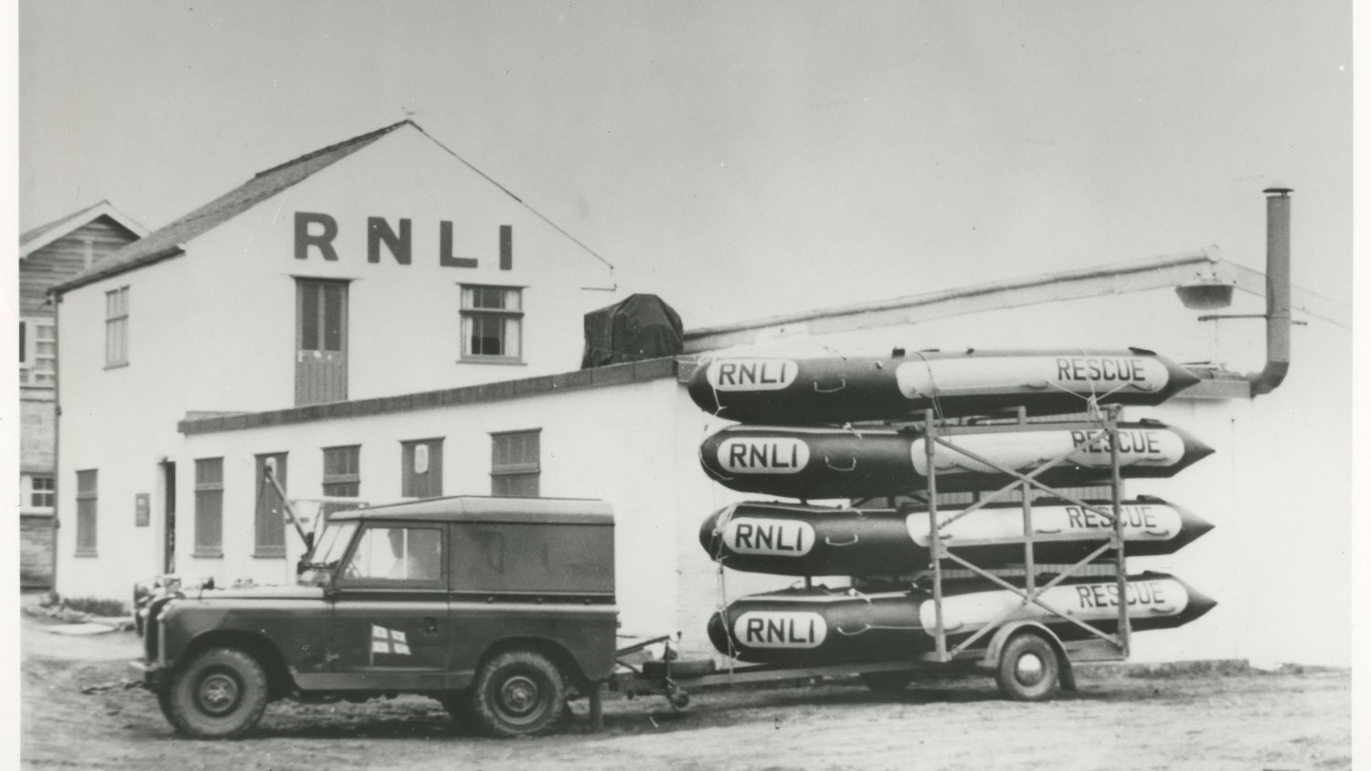Black and white image of landrover with four inflatable rescue boats on trailer