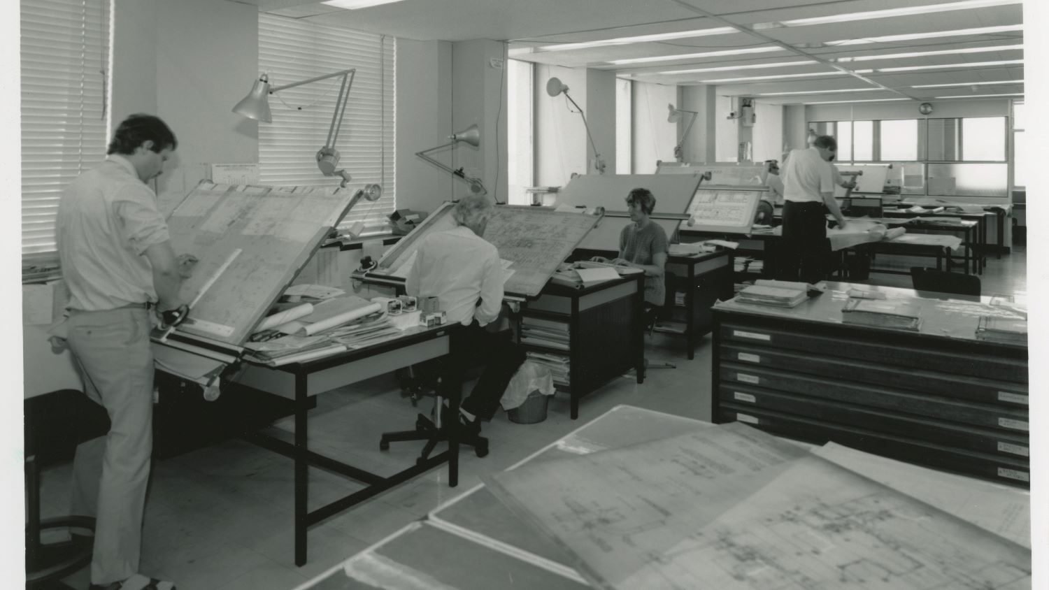 Black and white image of drawing office interior with staff at drawing boards