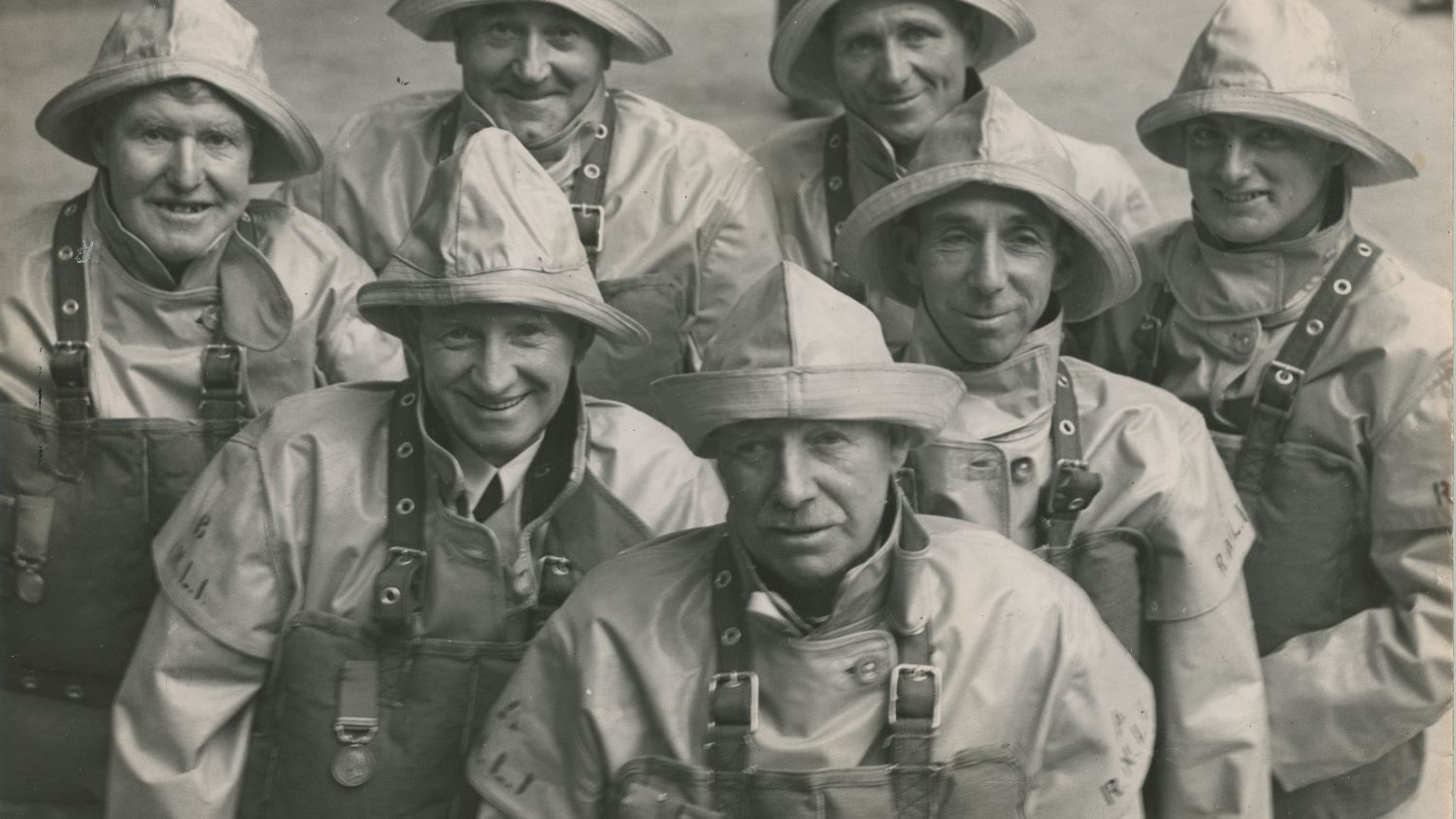Black and white image of seven men in crew kit with medals
