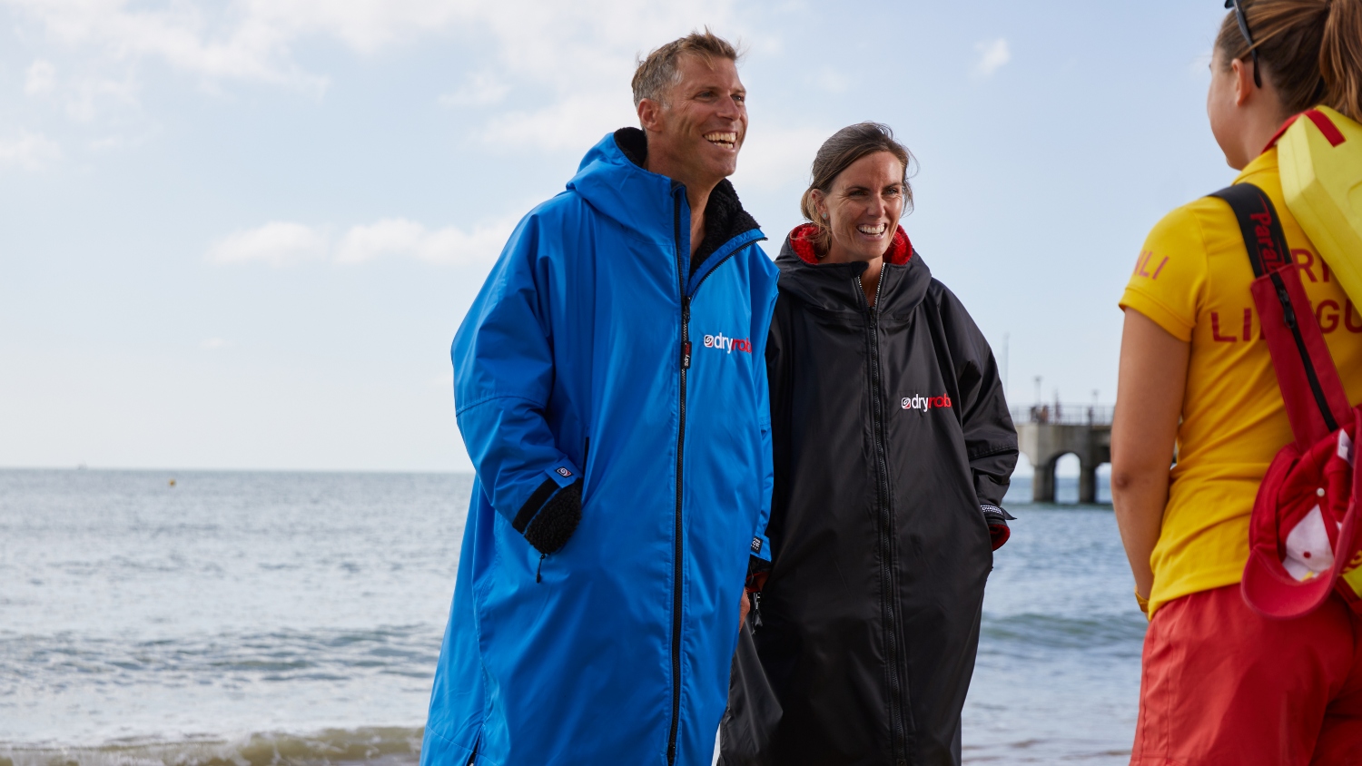 Man and woman in dryrobes smiling at an RNLI LIfeguard