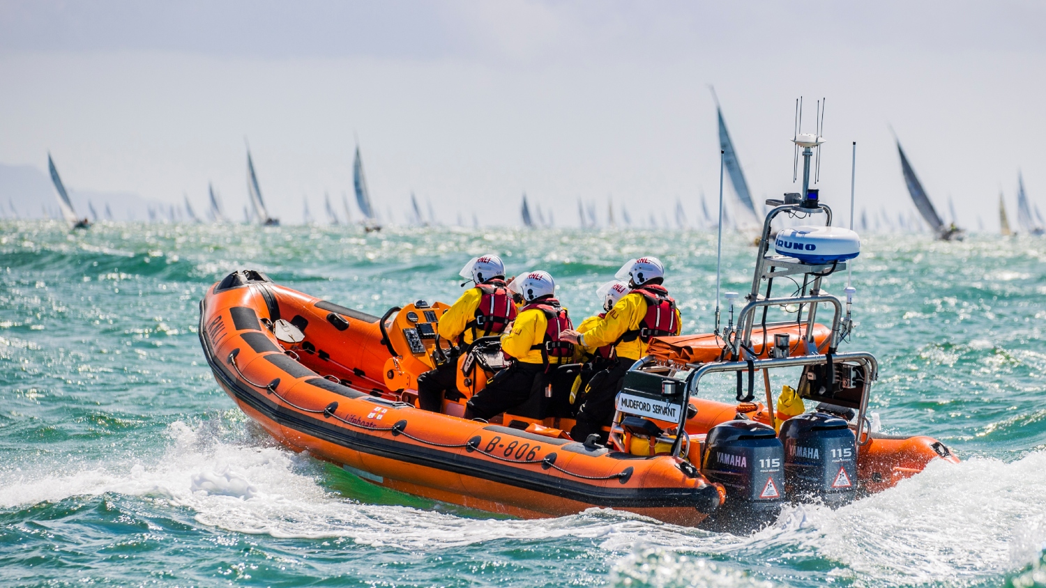 Mudeford inshore lifeboat provides safety cover at the Round the Island Race 2022. The orange lifeboat is in the foreground, while countless sailboats are seen in the background. 