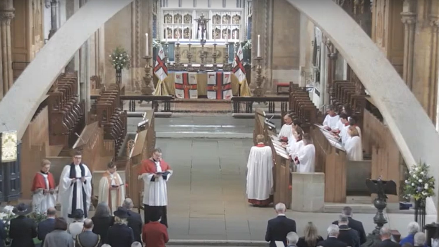 Inside Llandaff Cathedral during the RNLI Service of Thanksgiving on 27 April 2024. The clergy, choir and people in pews are standing and RNLI flags adorn the altar. 