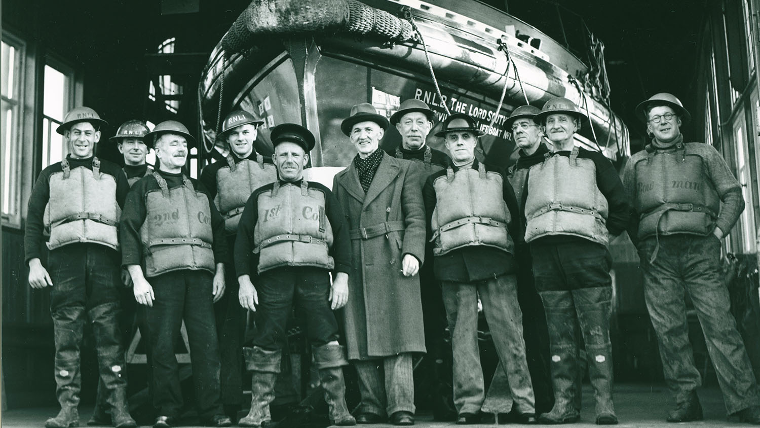 RNLI lifesavers during the Second World War. They are smiling at the camera and standing in front of a lifeboat.