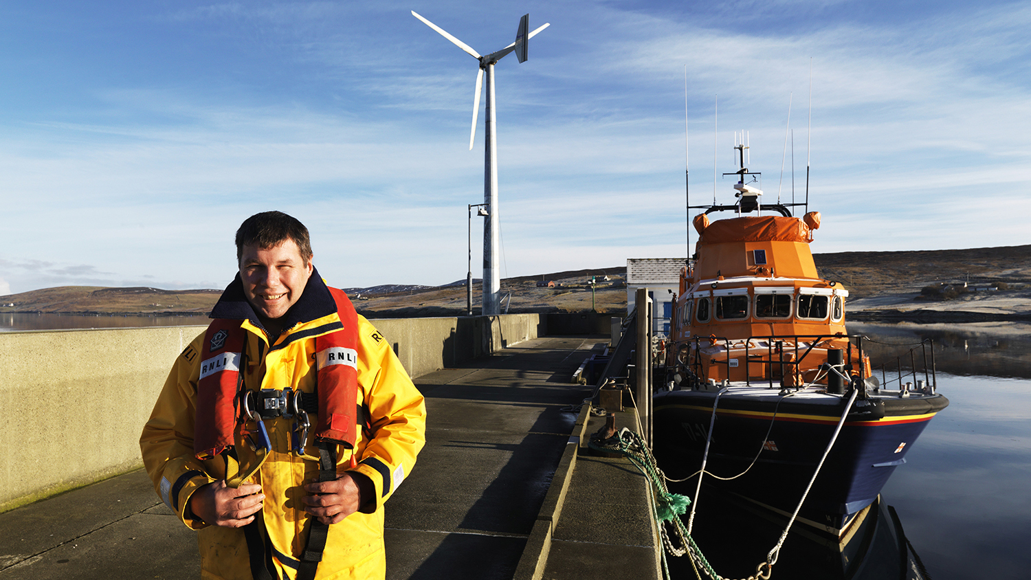 RNLI Mechanic Kevin Henry standing near Aith’s all-weather lifeboat and the station’s 20kW wind turbine