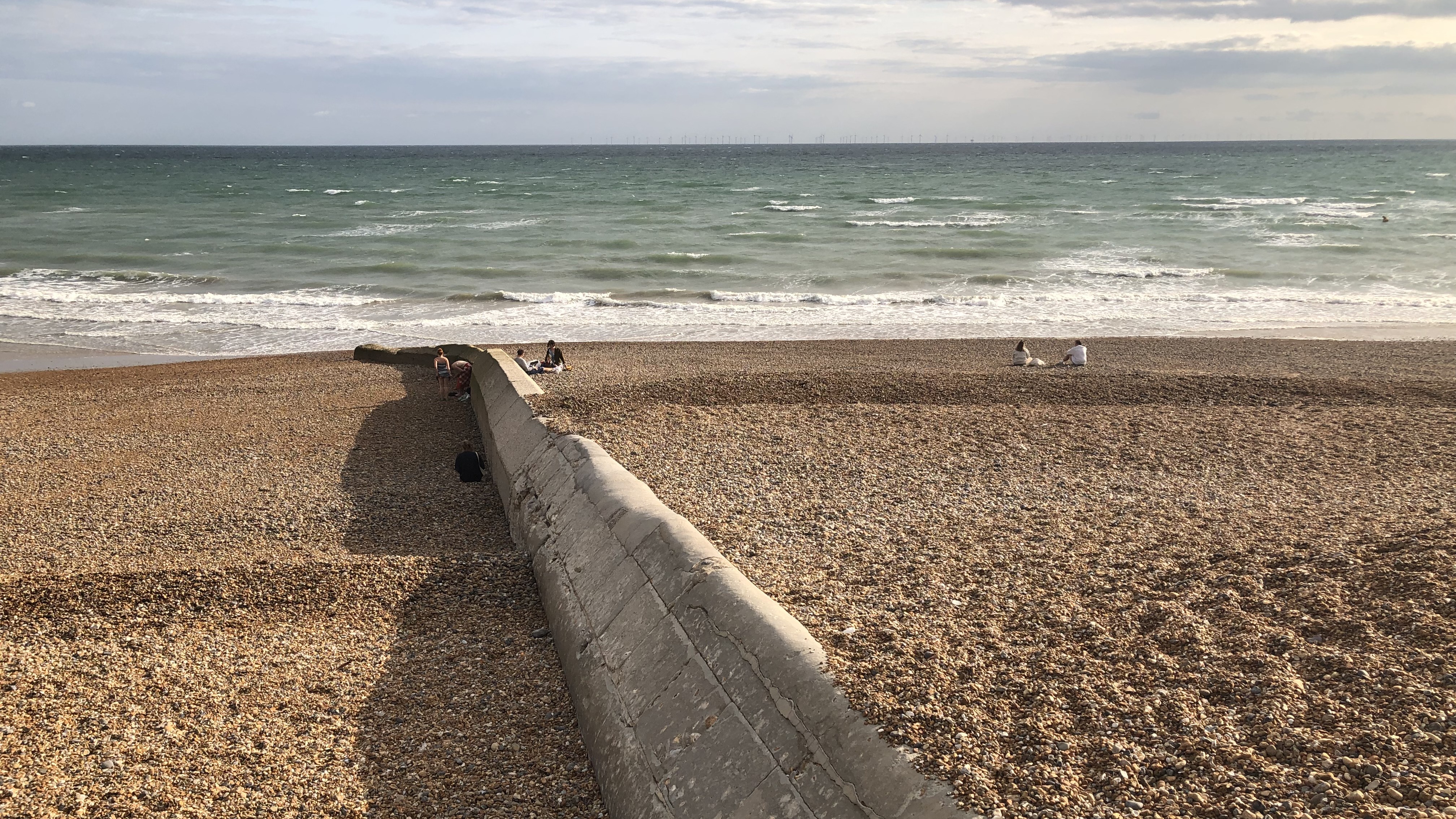 Image shows a pebbled beach looking out to the sea on an overcast day. A stone groyne runs through the middle of the beach. 