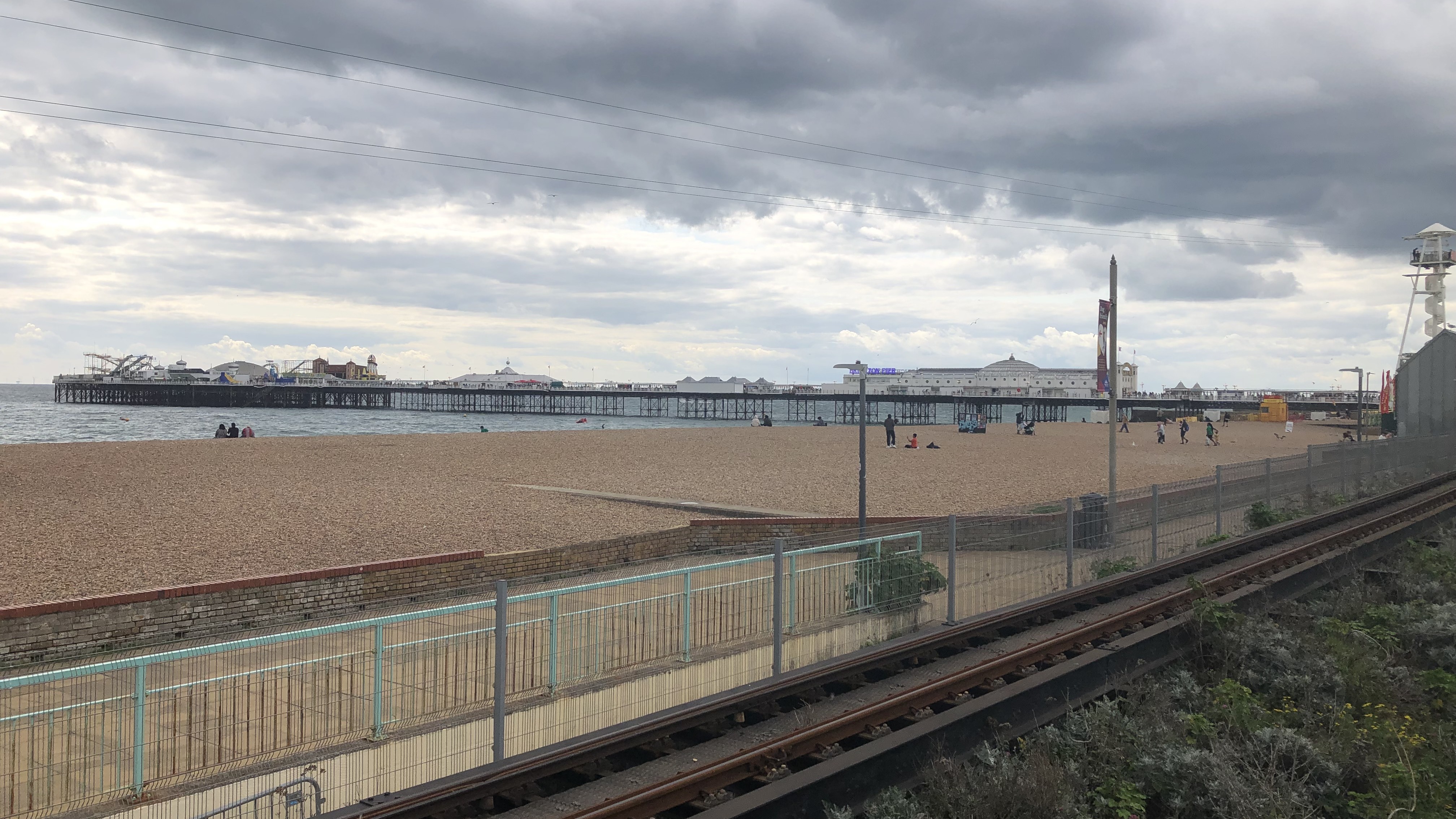 A landscape image of Palace Pier East Beach on an overcast day. The beach is pebbled, and in the distance Brighton Pier can be seen. 