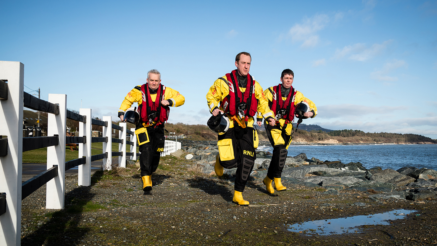 Three crew members, in full kit, run towards the camera