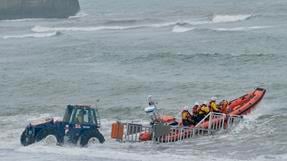 A lifeboat with four crew members is being launched into the sea by a tractor.