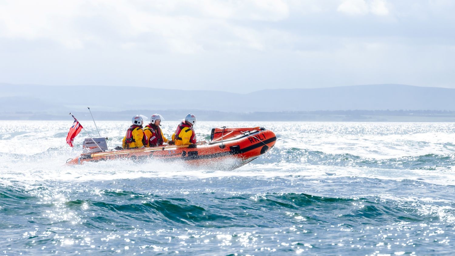 A small rib with three crew on blue seas reflecting the sunlight.