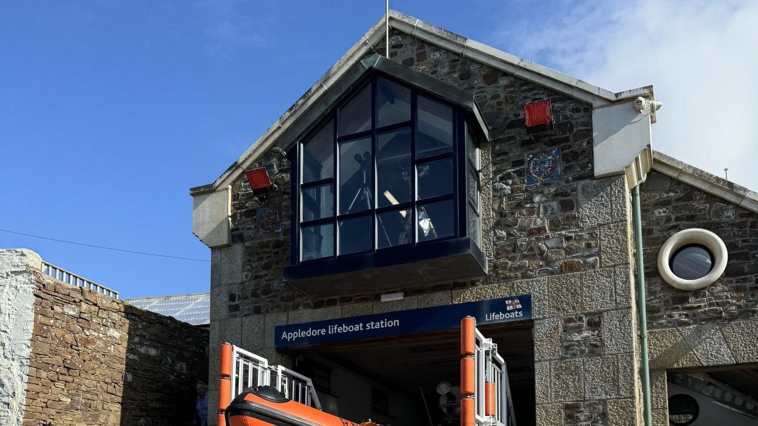 A two storey stone building with an open door to the boat shed at the bottom and a large floor-to-ceiling window upstairs.