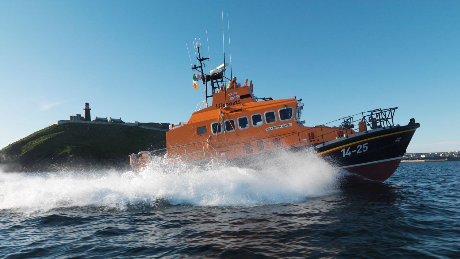 Ballycotton Trent Class lifeboat Austin Lidbury 14-25 moving from left to right, lighthouse in the background. Bright sunny day, blue sky.