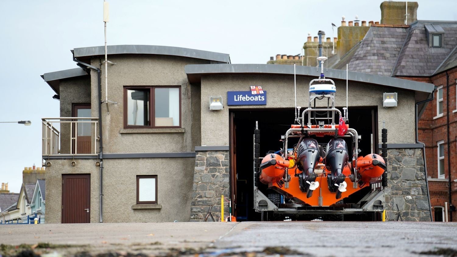 A grey building with curved roof and an inshore lifeboat partially out of the boatshed.