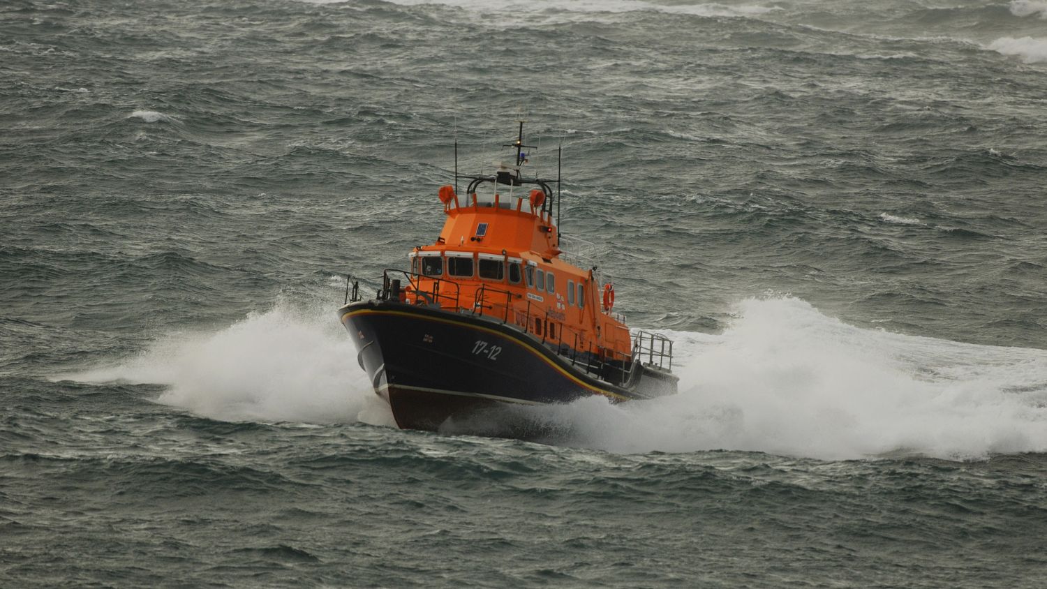 Barra Island Severn class lifeboat Edna Windsor moving towards the camera in dark choppy seas, throwing up white spray. 