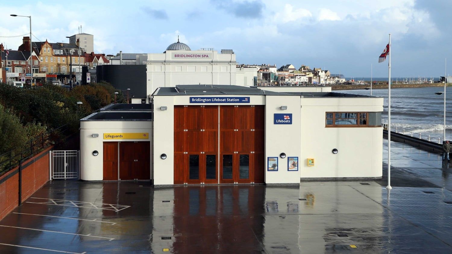 A white building on the sea front with large wooden doors to a boatshed and smaller wooden doors labelled lifeguards.