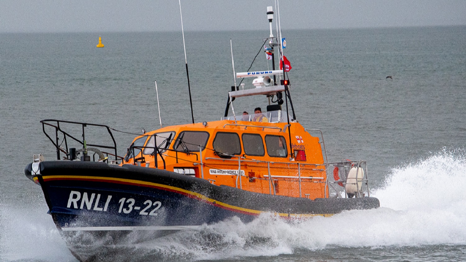 An orange and dark blue RNLI lifeboat powers through grey, choppy waters.
