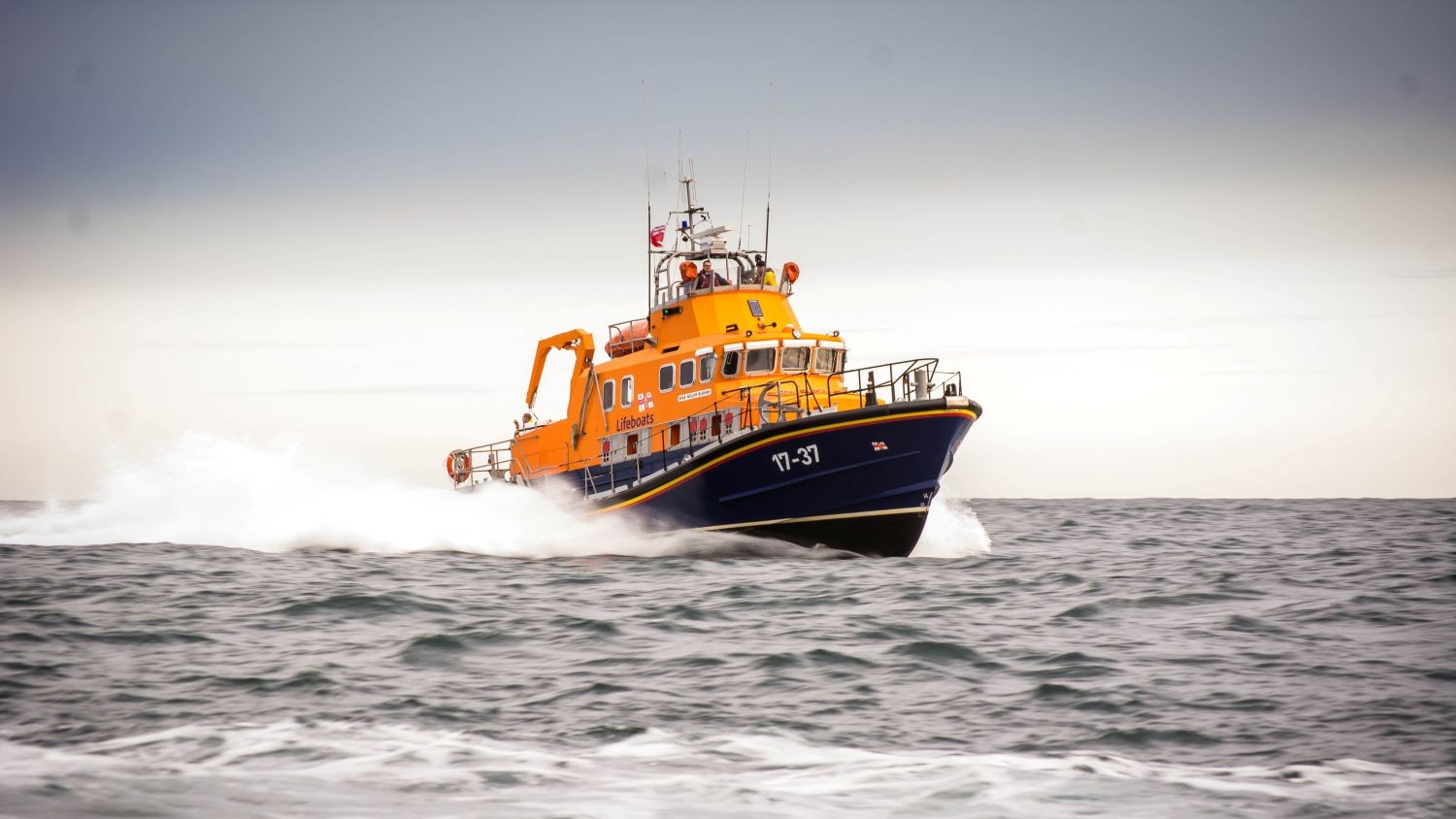 A Severn class all weather lifeboat creating spray on grey water.