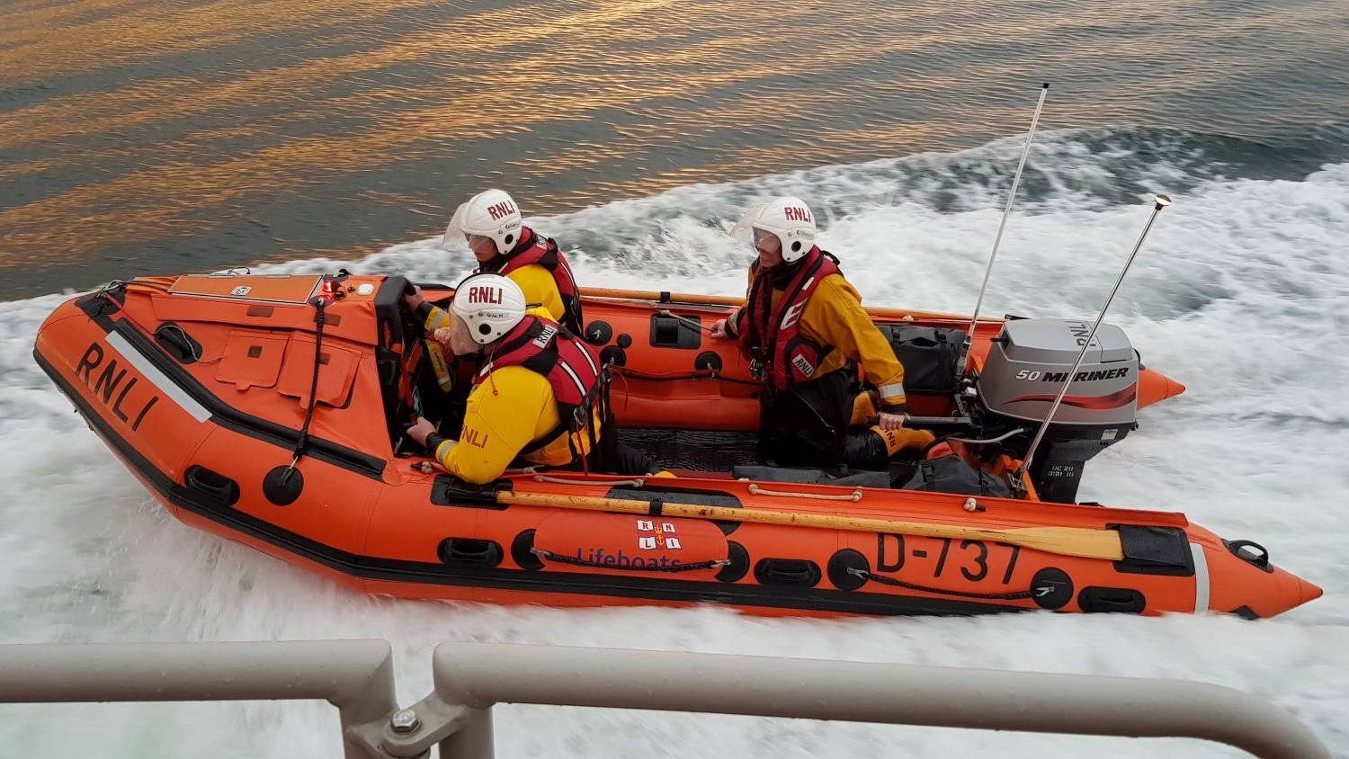 A small rib with three crew onboard alongside a larger boat.