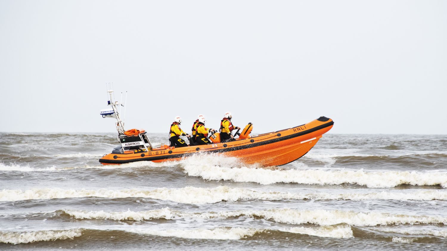 A b class  lifeboat, with four crew members, in choppy water on an overcast day.