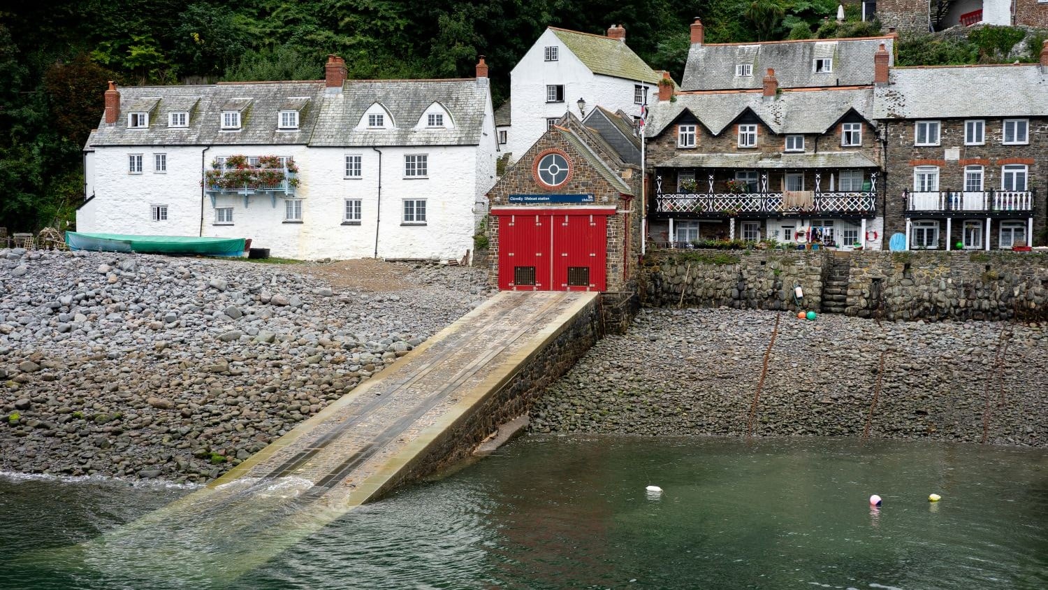 A small stone boathouse with a red door and a long slipway.