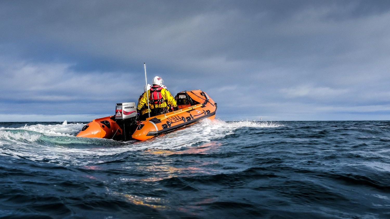A small rib with three crew members on dark blue water.