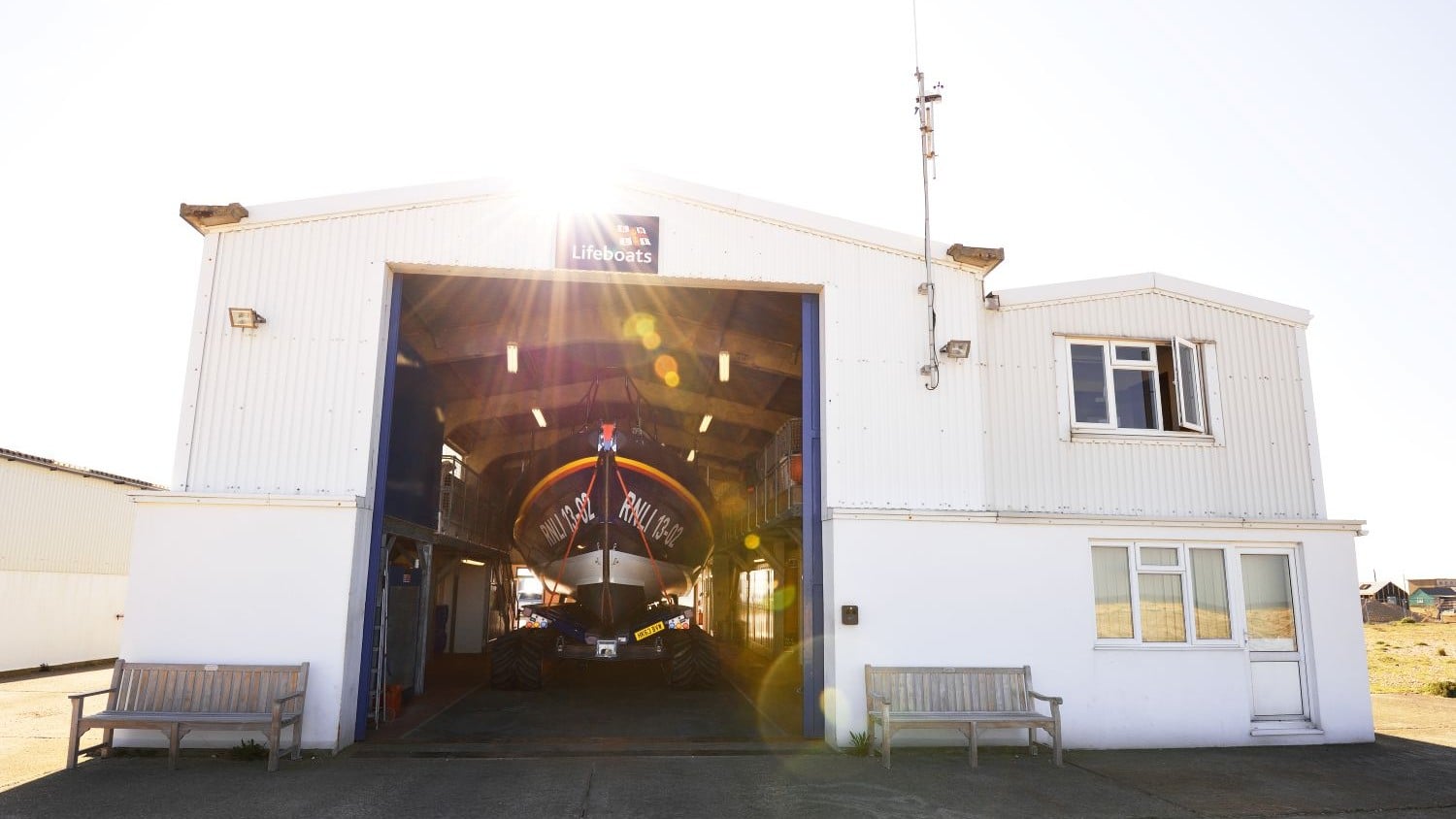 A large white building with two-storey high doors open to show the boat on it's launch and recovery system inside.