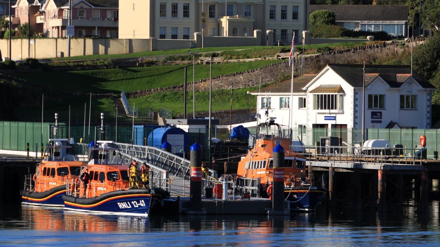 A two-storey white building with a jetty where three all weather lifeboats are moored.