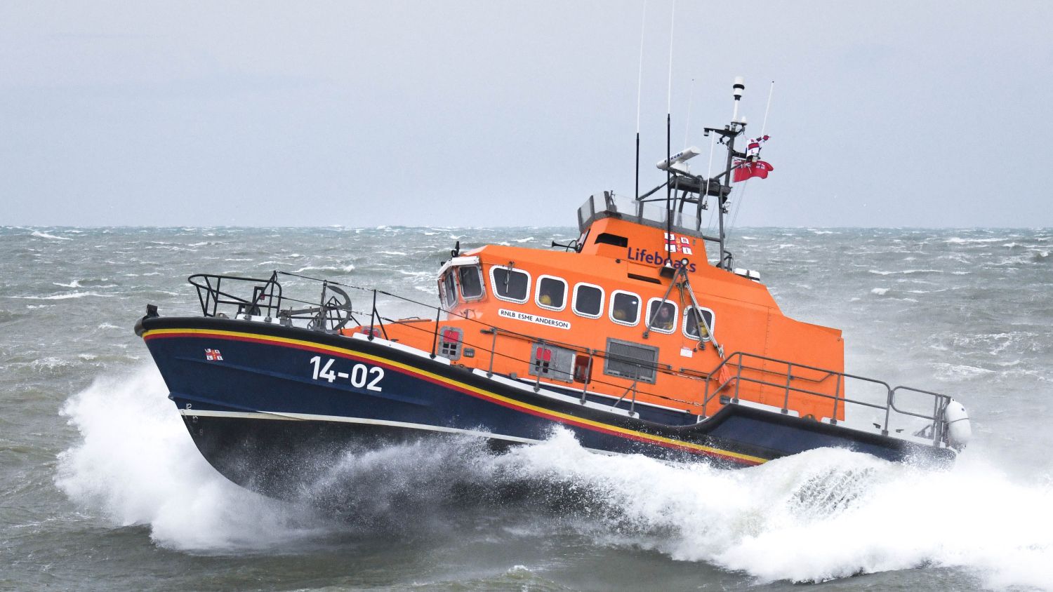 A lifeboat marked moves through choppy water, creating spray along the hull.