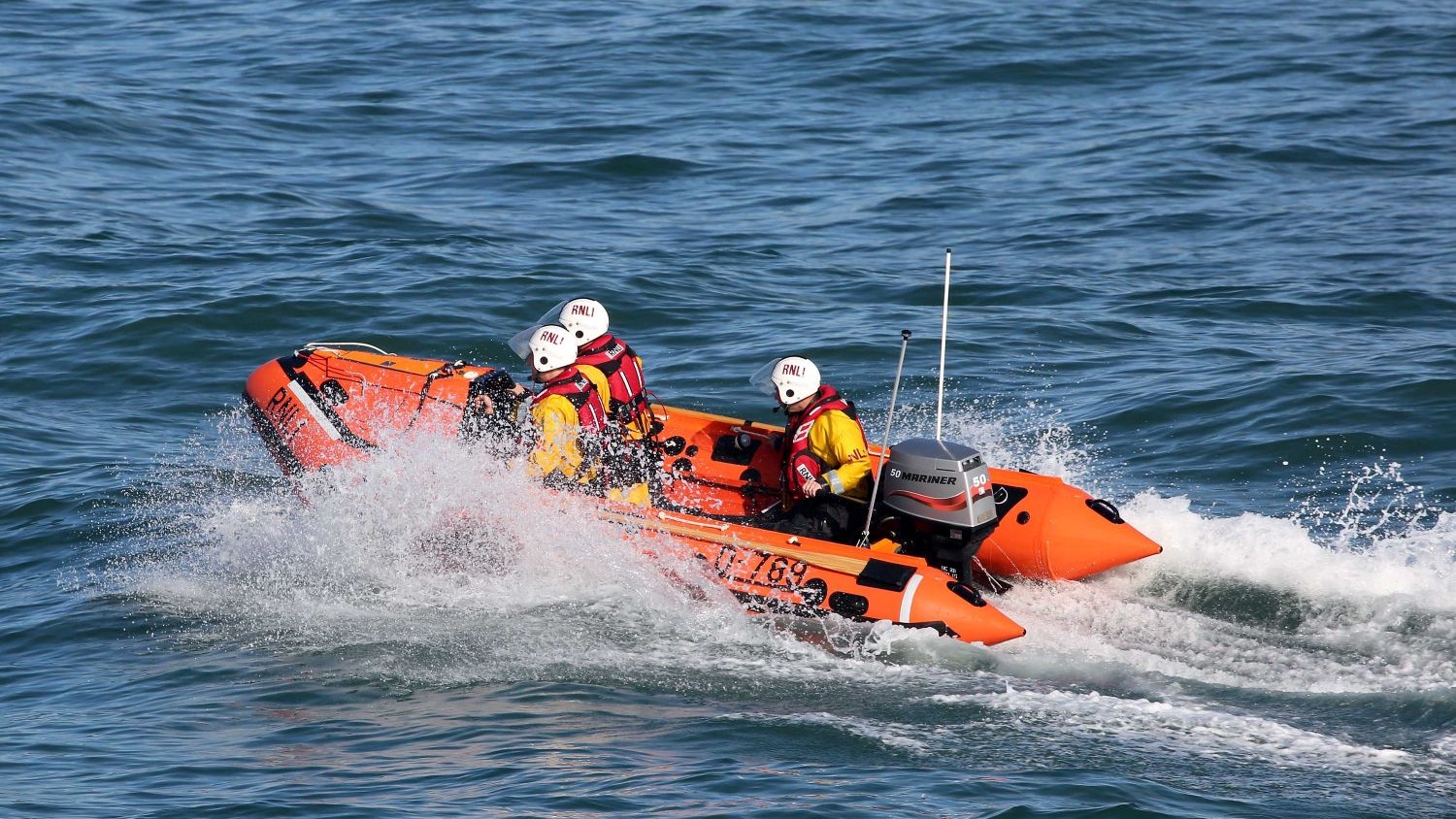 A small rib with three crew creating spray on blue water.