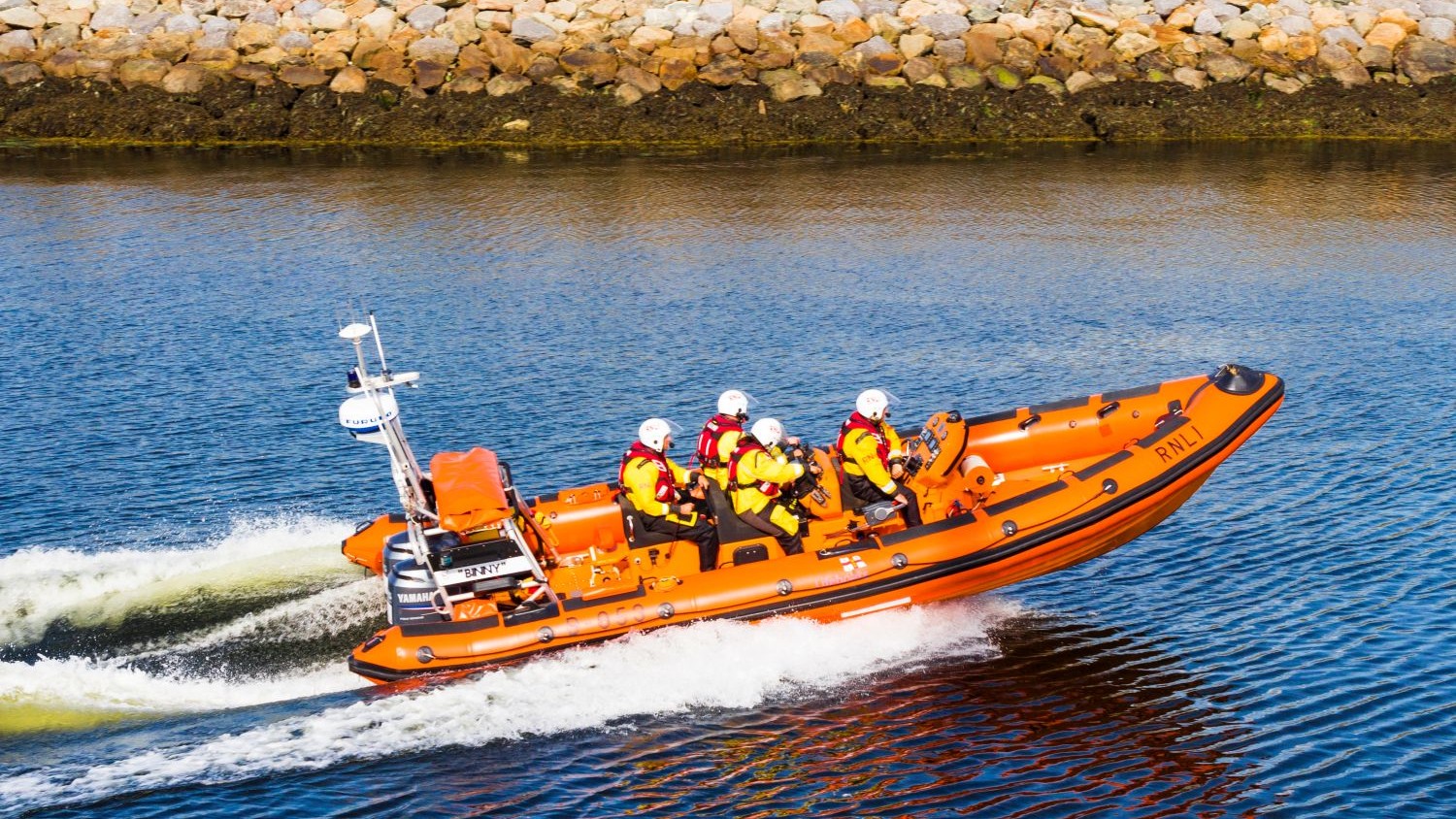 The Galway lifeboat creating a wake in calm water on a sunny day.