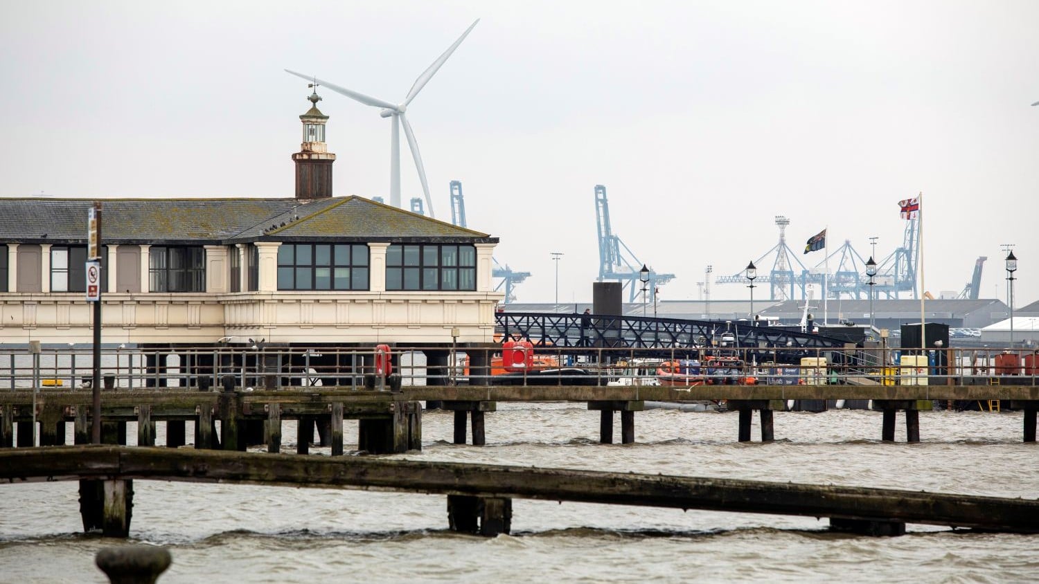 A enclosed wooden pier with cranes and a windmill behind it.